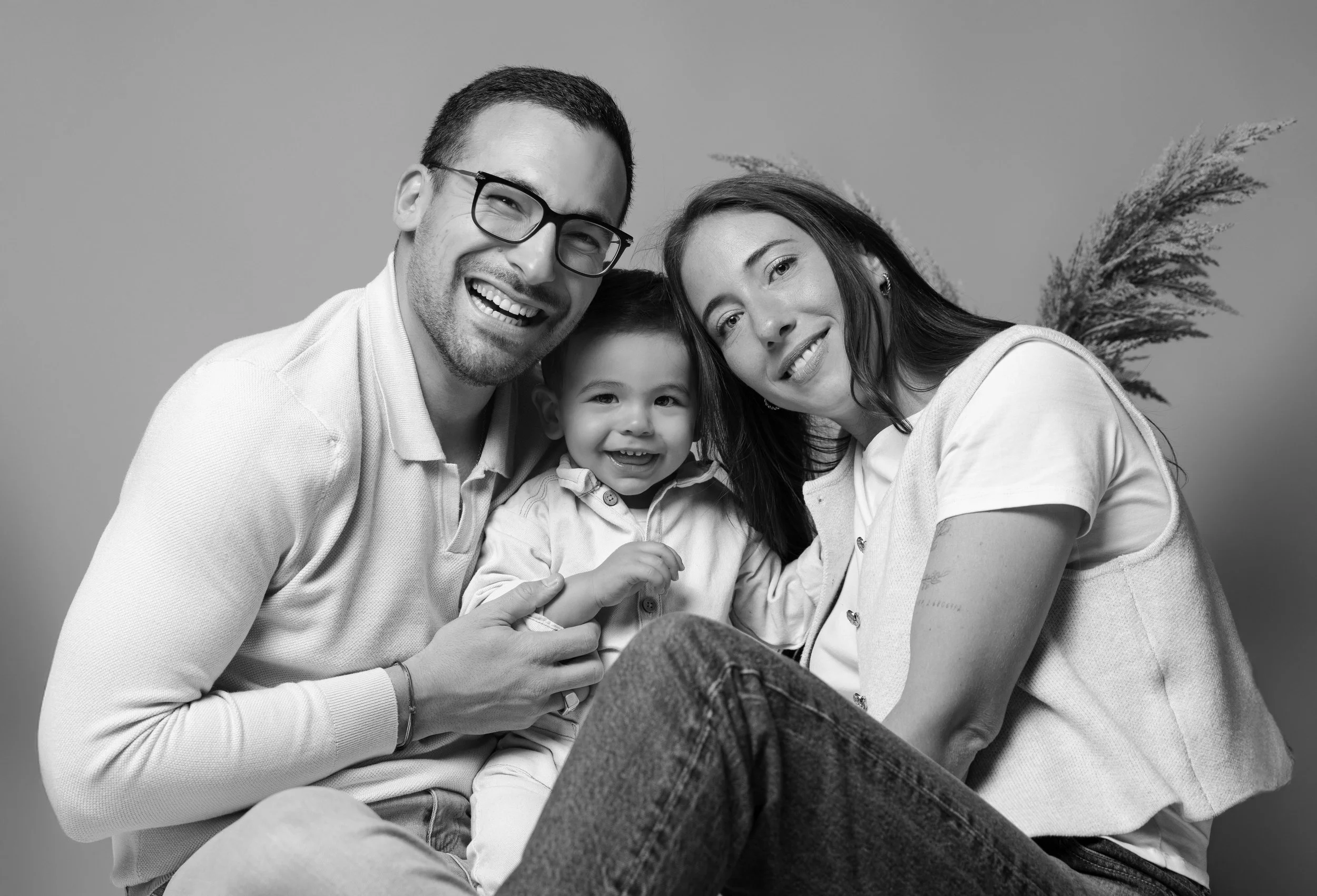 Photo en noir et blanc d’un couple souriant avec leur enfant, tous les trois serrés ensemble, dans une ambiance chaleureuse.