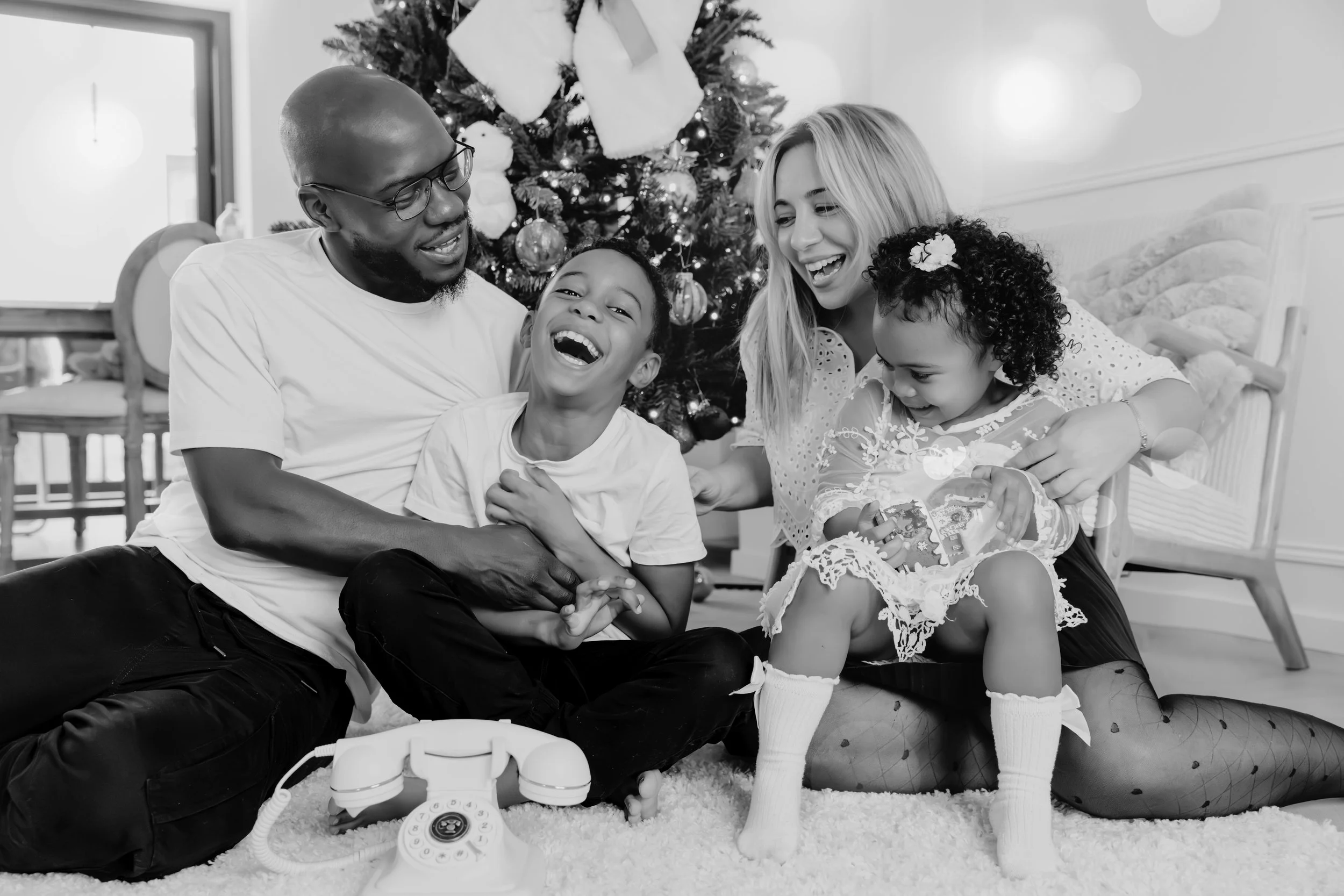 Une famille de quatre personnes, un père, une mère, un fils et une fille, souriant et jouant ensemble près d'un arbre de Noël décoré.