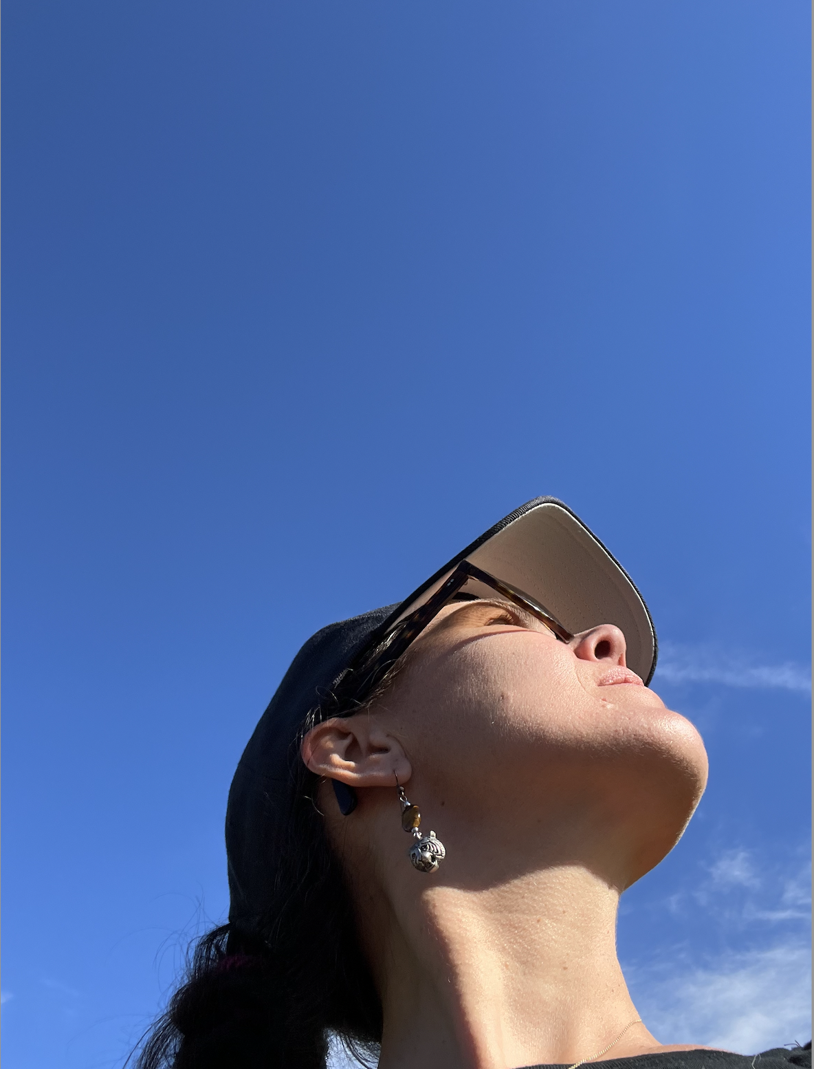 Junge Frau trägt Sonnenbrille und Baseballcap, schaut nach oben gegen blauen Himmel
