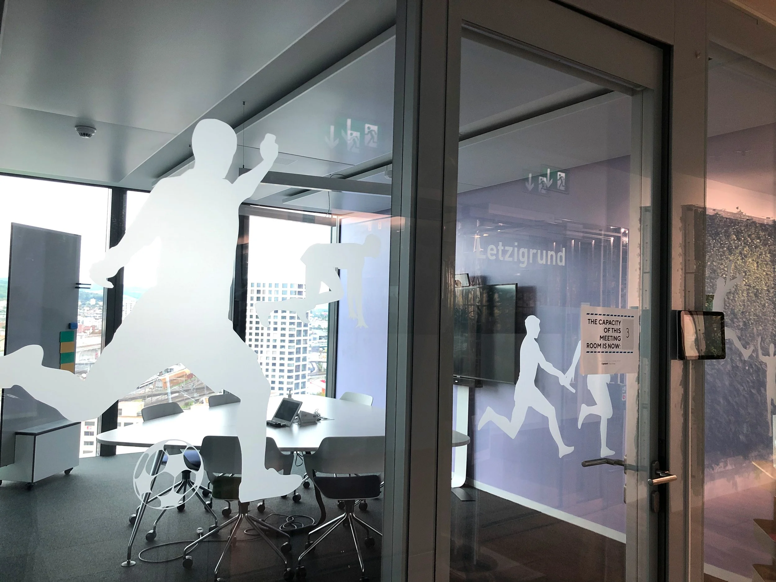 Fenster mit weißen Aufklebern von Kindern, die verschiedene Aktivitäten wie laufen, klettern und spielen zeigen, in einem modernen Büro.