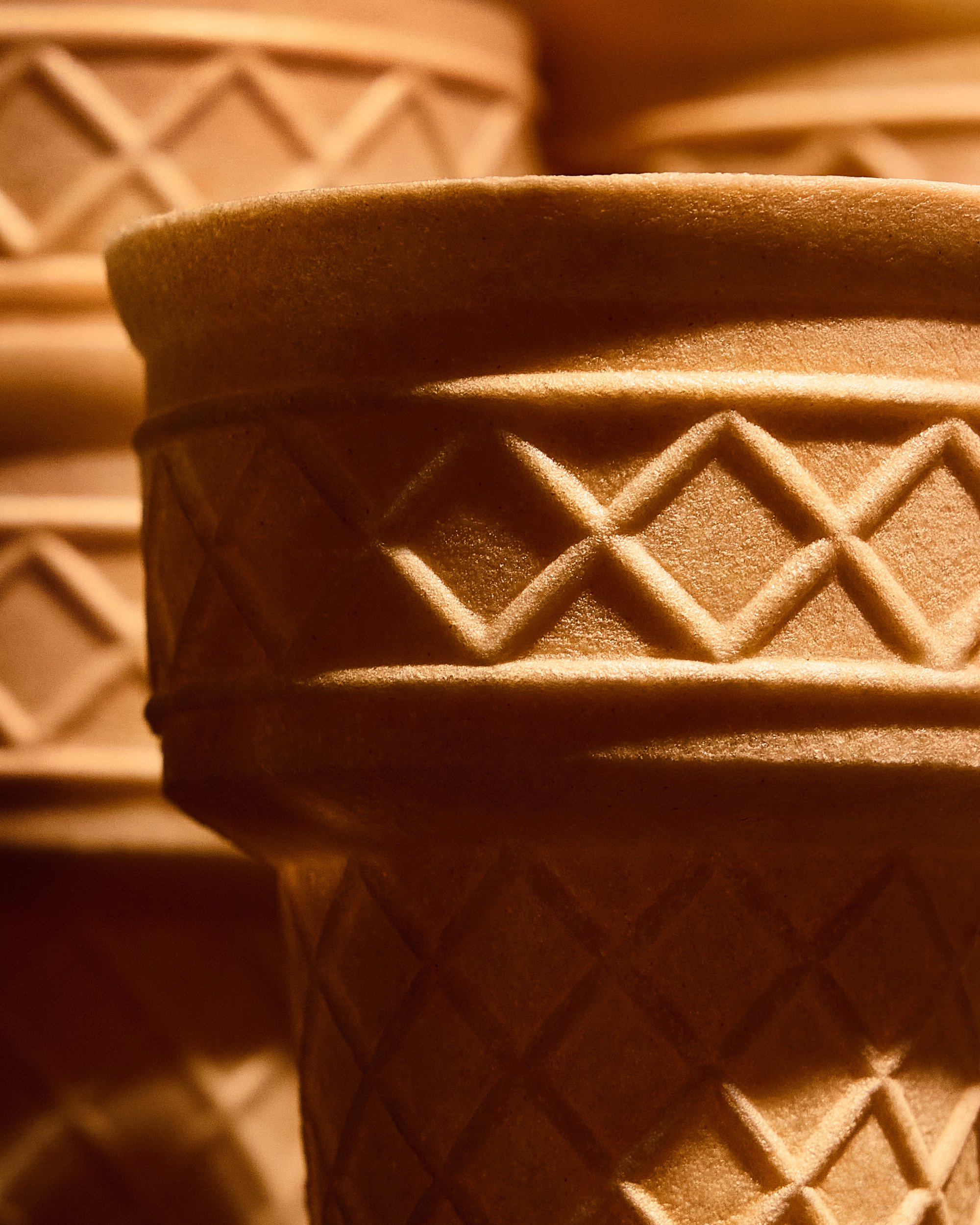 Close-up of a textured, brown ice cream cone with a decorative diamond pattern, with other blurred cones in the background.