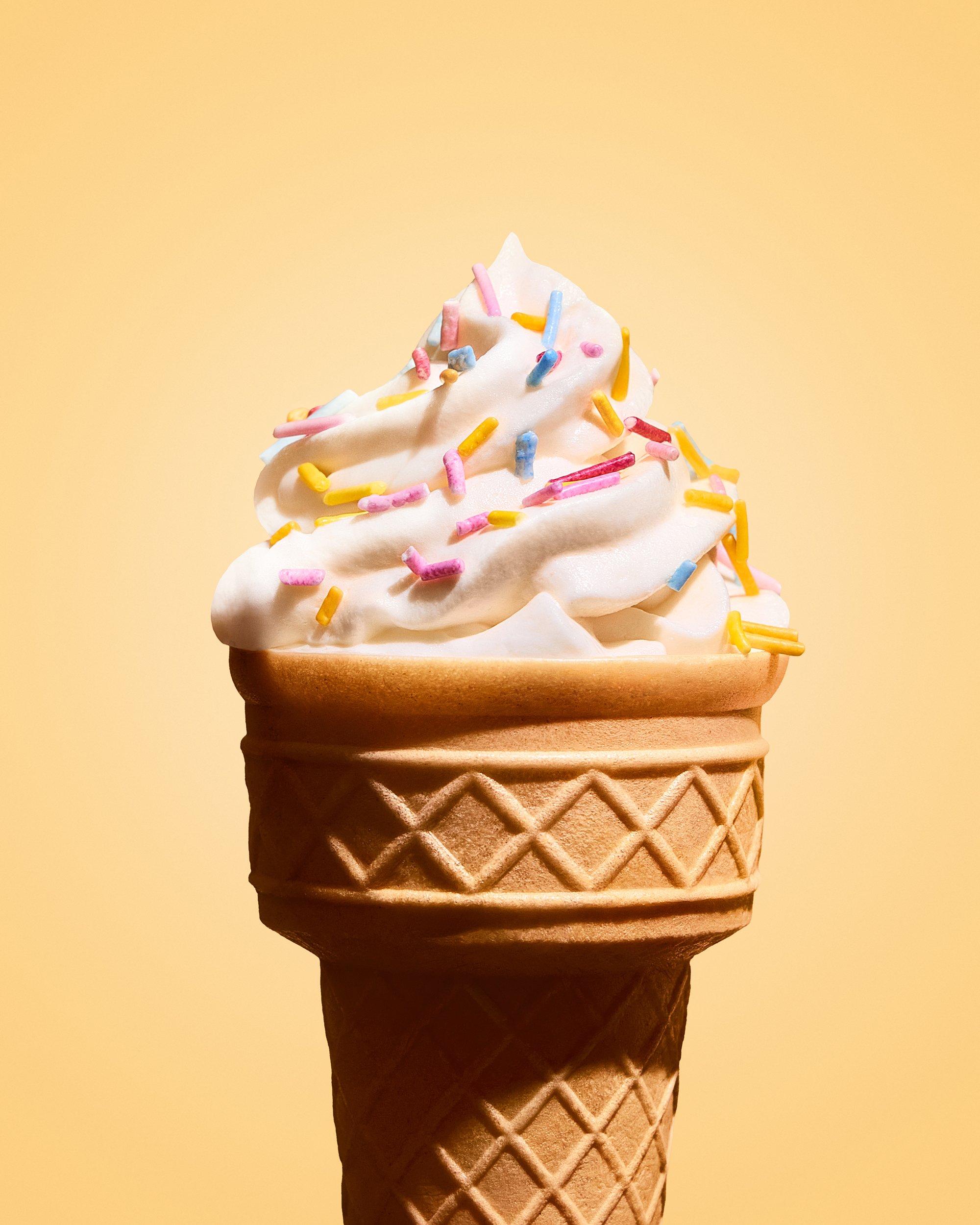 Close-up of a vanilla ice cream cone topped with colorful sprinkles against a yellow background.