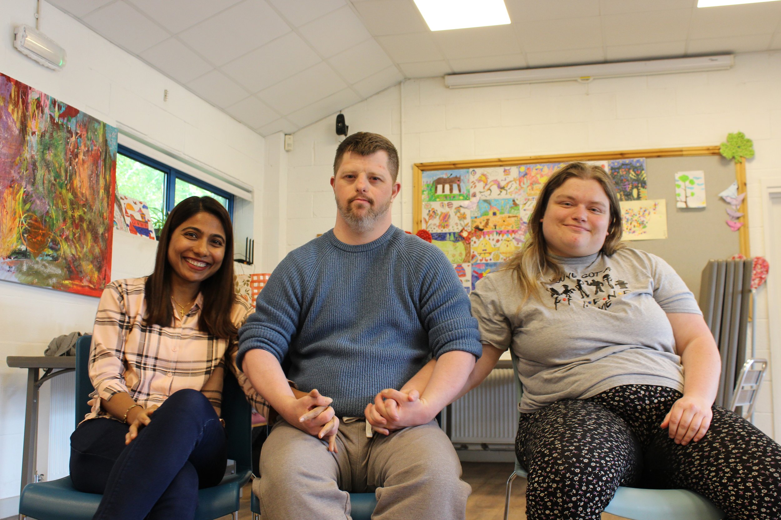 Three people sitting down linking arms and smiling