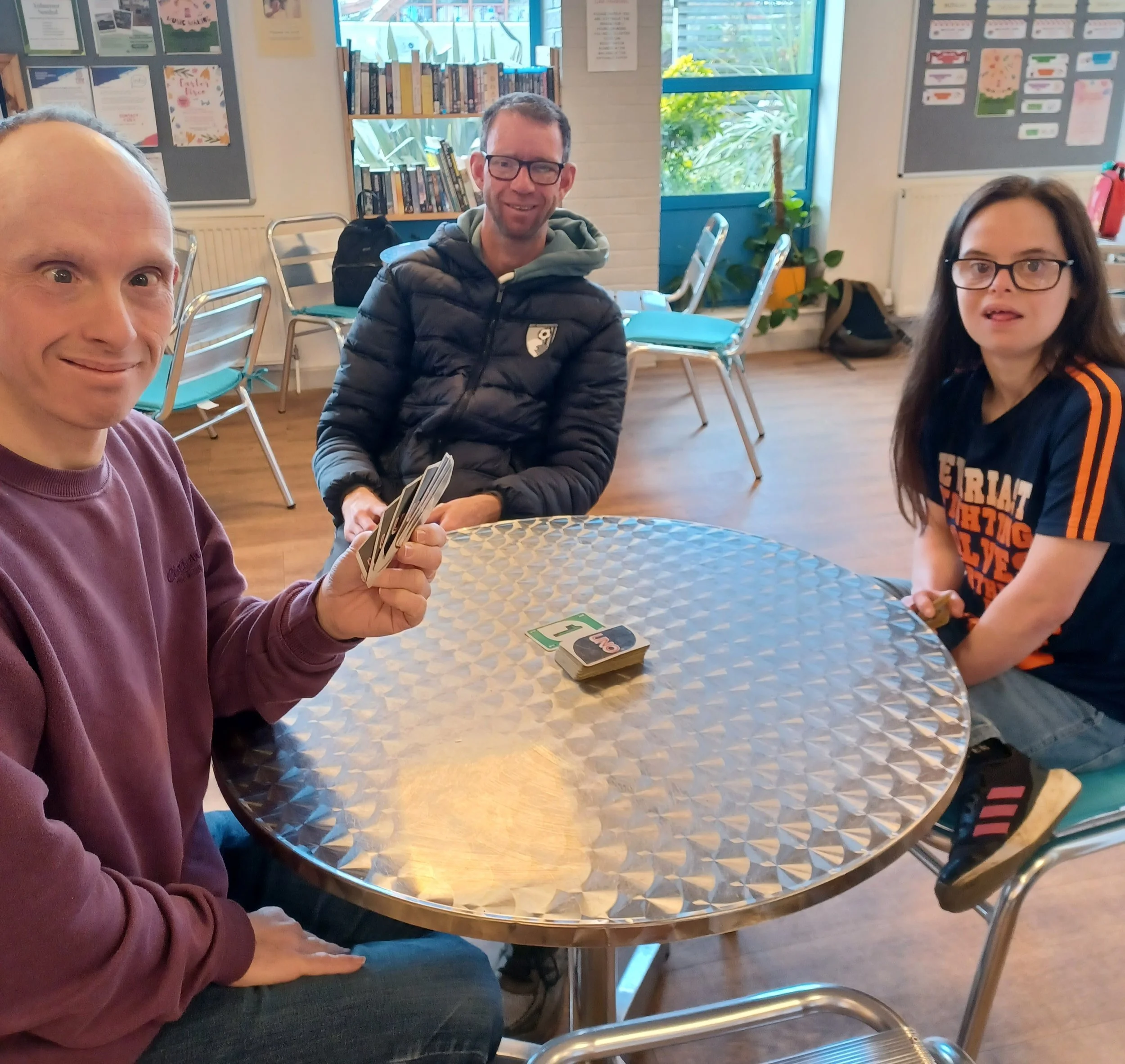 Three people sitting around a table playing card game