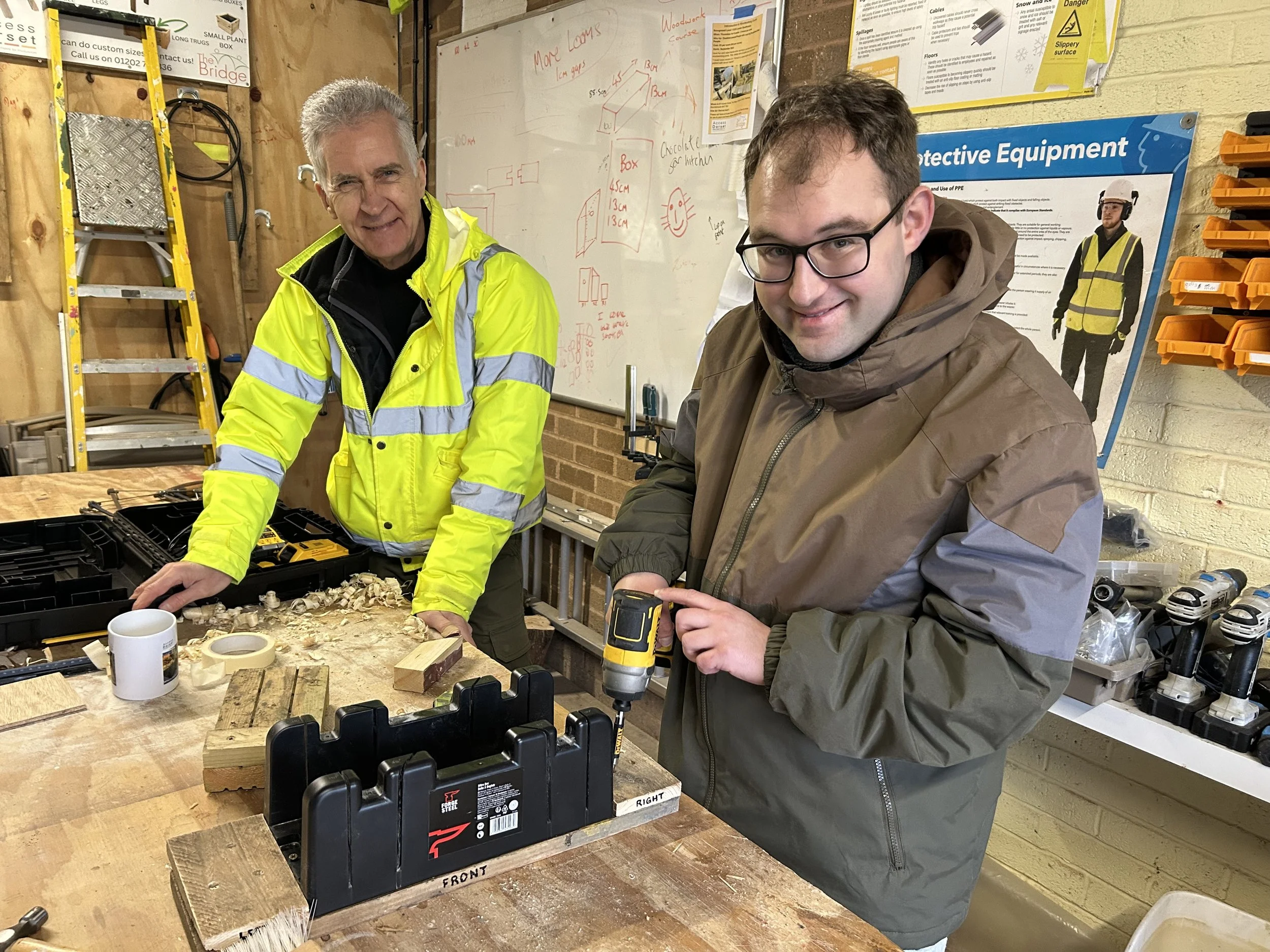 Two smiling men standing in a workshop surrounded by DIY equipment