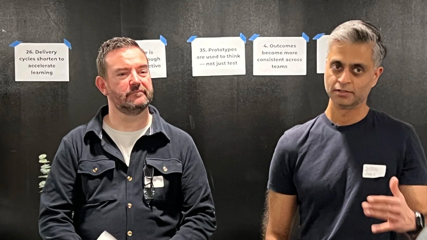 Kursholdere David og Jiten står foran en sort vegg som det henger sitater på. Foto.