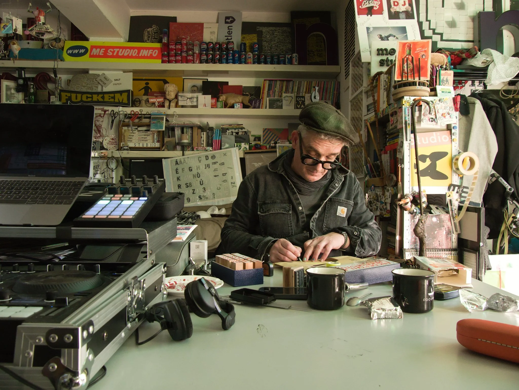 Designer Martin Pyper drawing at a table in his Amsterdam studio. There is tons of stuff around him including DJ decks and endless shelves of magazines and books.