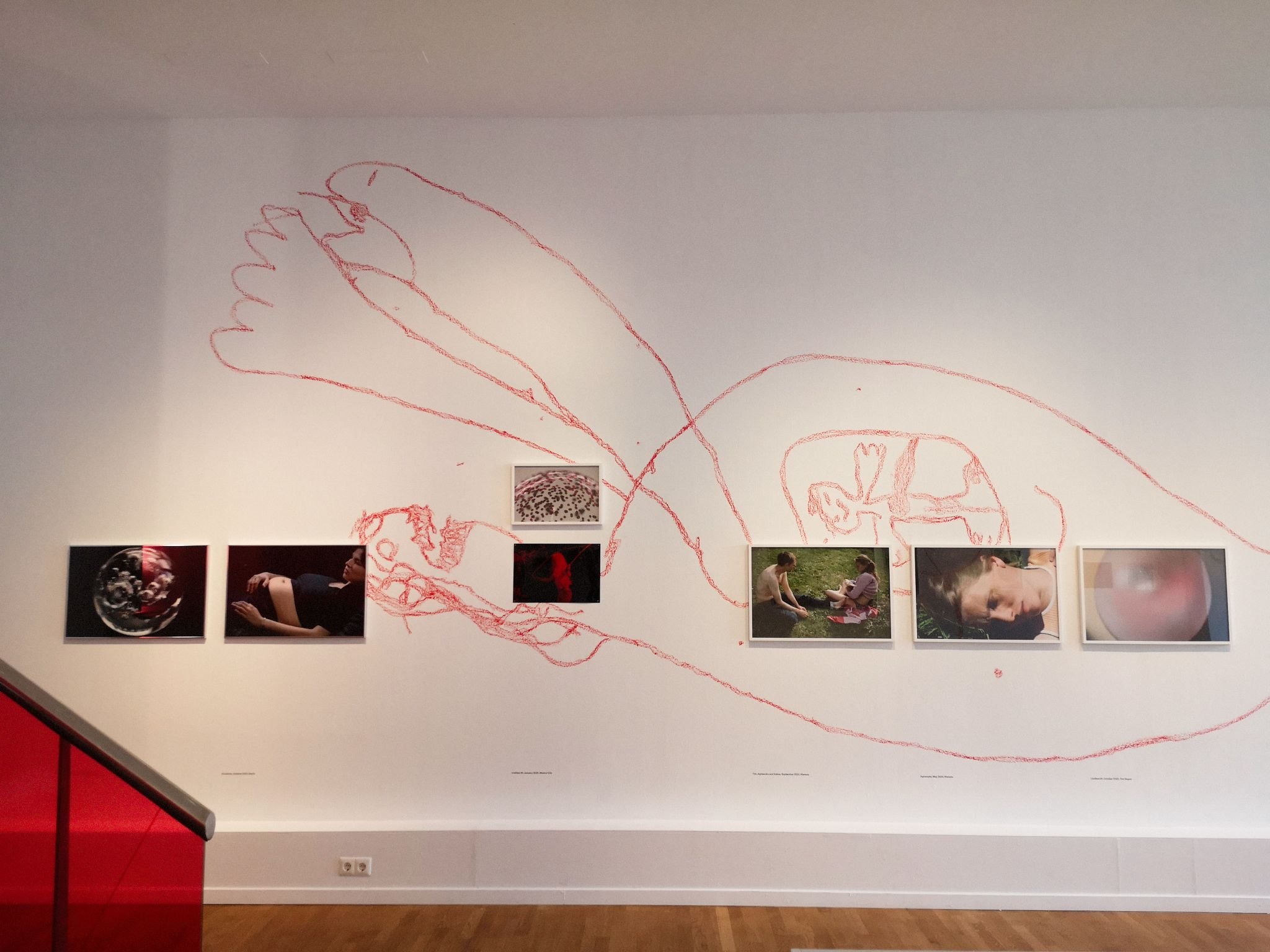 Wall at the Verena Blok exhibition. It features photos of women in various stages of pregnancy and abstract close ups of things connected to pregnancy. On the main white wall is a child's drawing of a pregnant woman with a baby in her tummy.