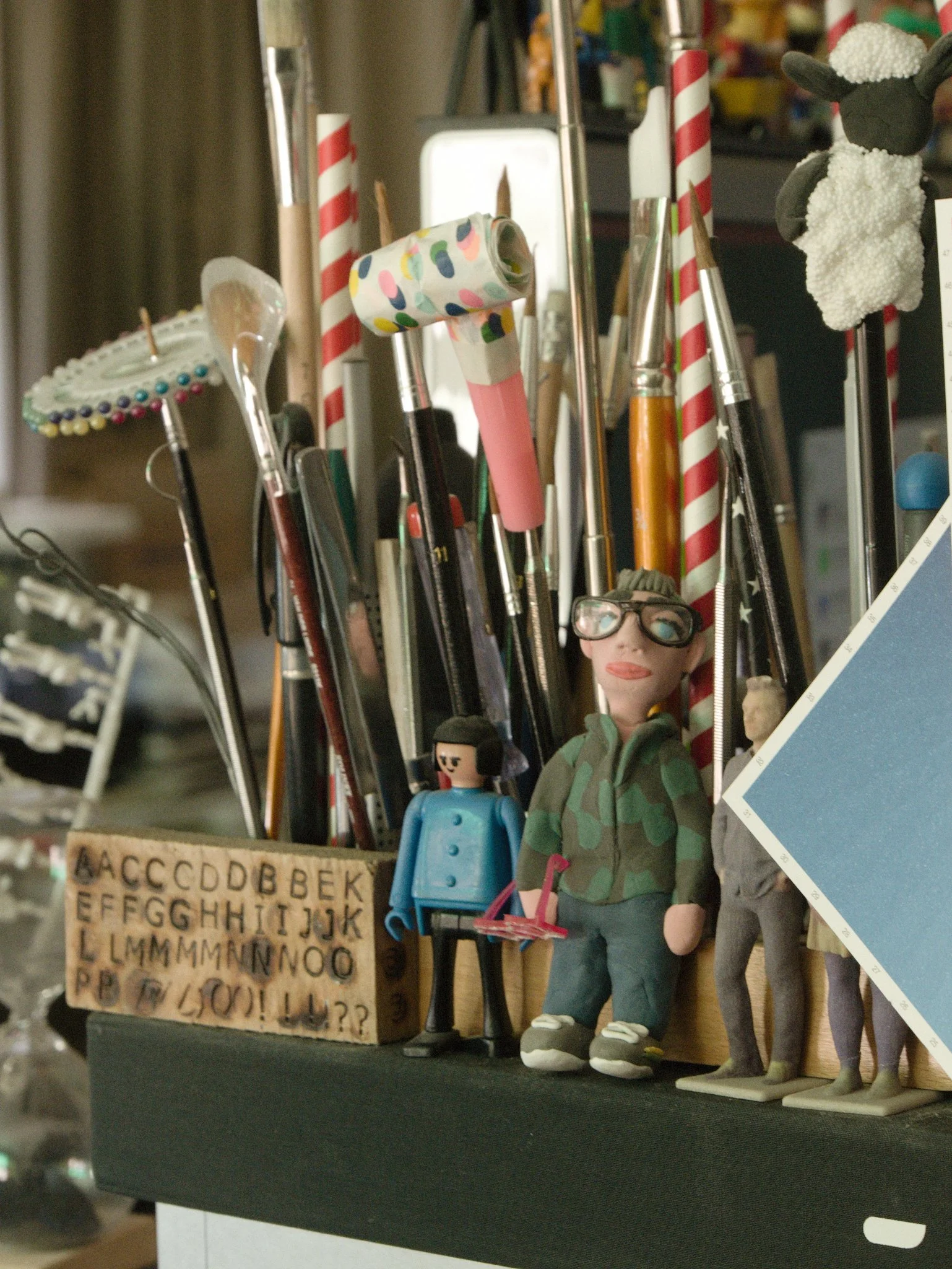 A plasticine model of Martin Pyper with several other figures standing next to a stack of paint brushes and letter stamps.