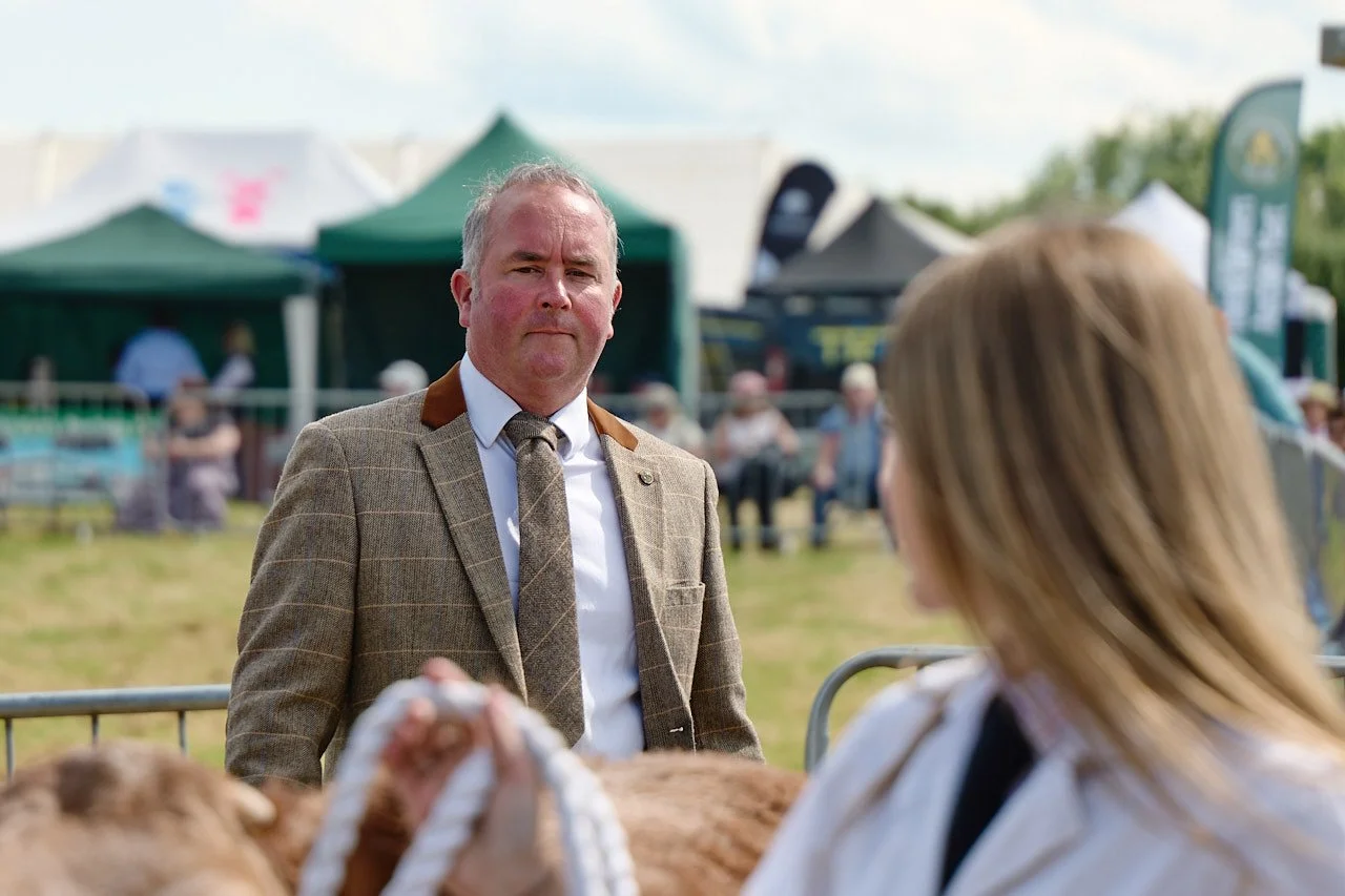 Close up of a judge during the cow competition. He is wearing a tweed jacket and tie and is in deep concentration.