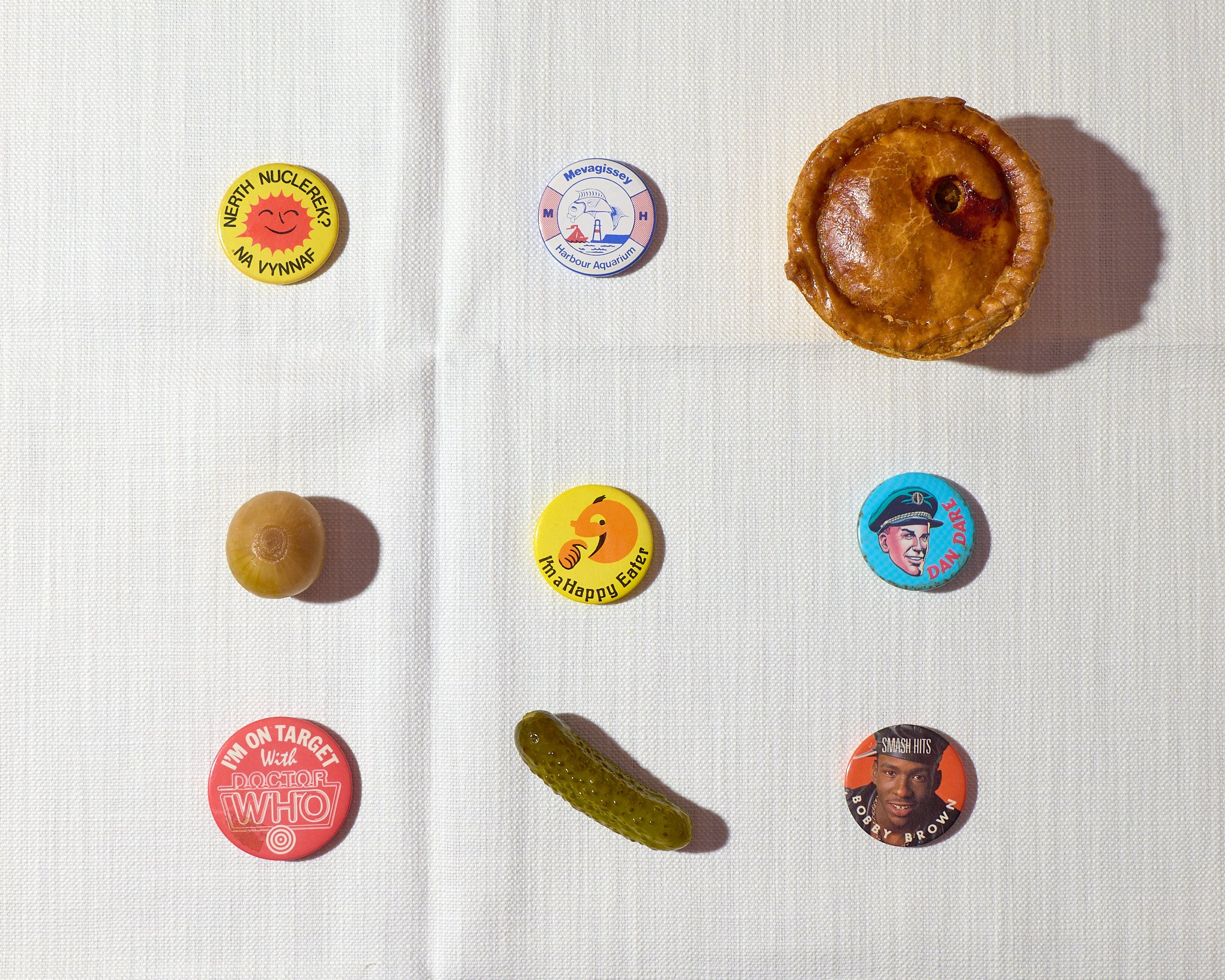 An array of badges and snacks including a pork pie, Dr Who, pickled onion and Happy Eater.