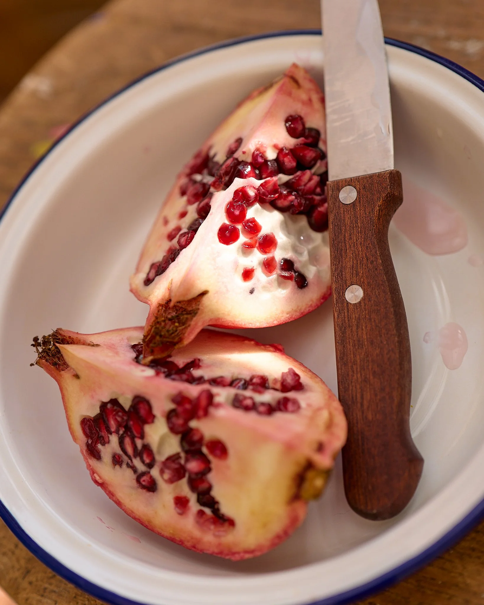 Food photography of a quartered pomegranate sitting in a bowl with a sharp knife.