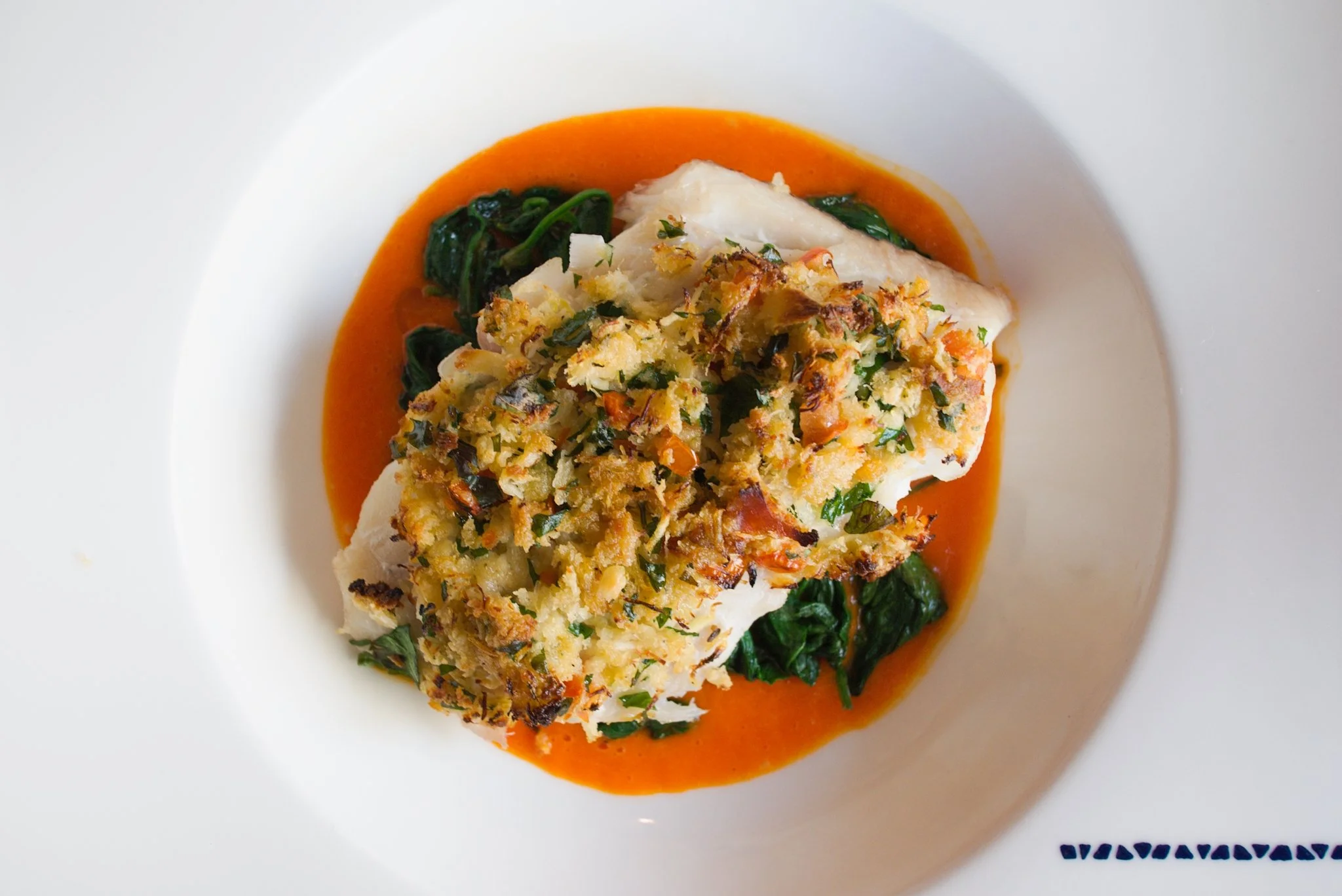 A top down view of a white fish dish with breaded topping and greens with red sauce on a white plate at the Drum and Monkey in Harrogate.