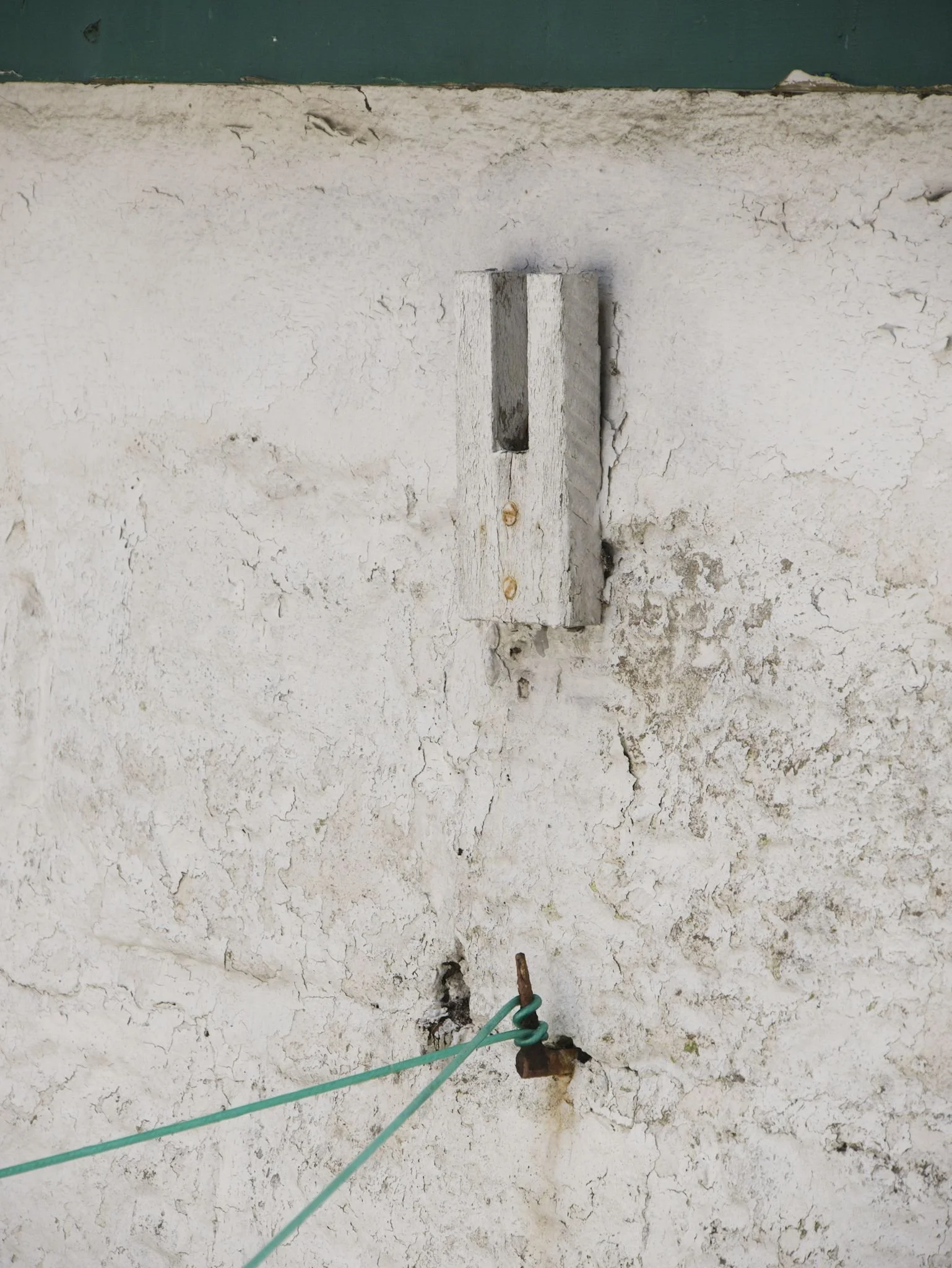 A white wall with a wooden beam prop and green washing line hanging off a hook.