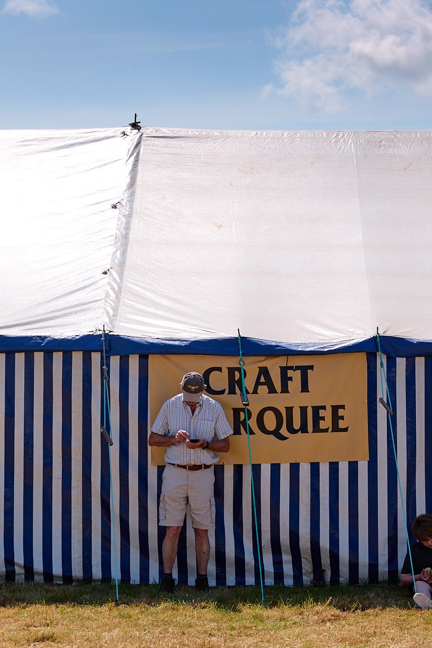 A man texting on his phone in the shade of the craft marquee during a hot summers day.