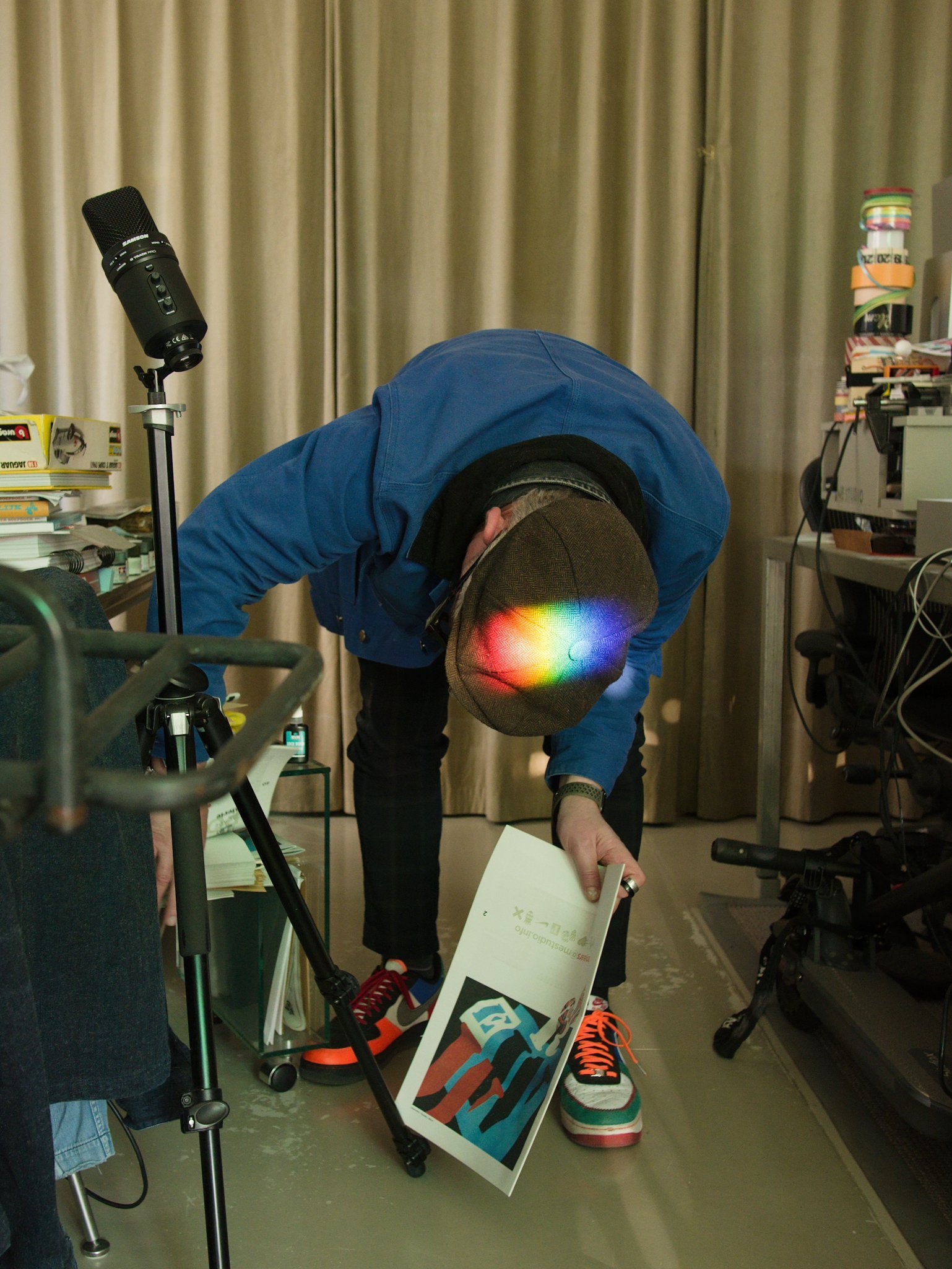 Portrait of designer Martin Pyper searching for something in his Amsterdam studio. Light is refracting on his cap as he bends over to rummage in a drawer.