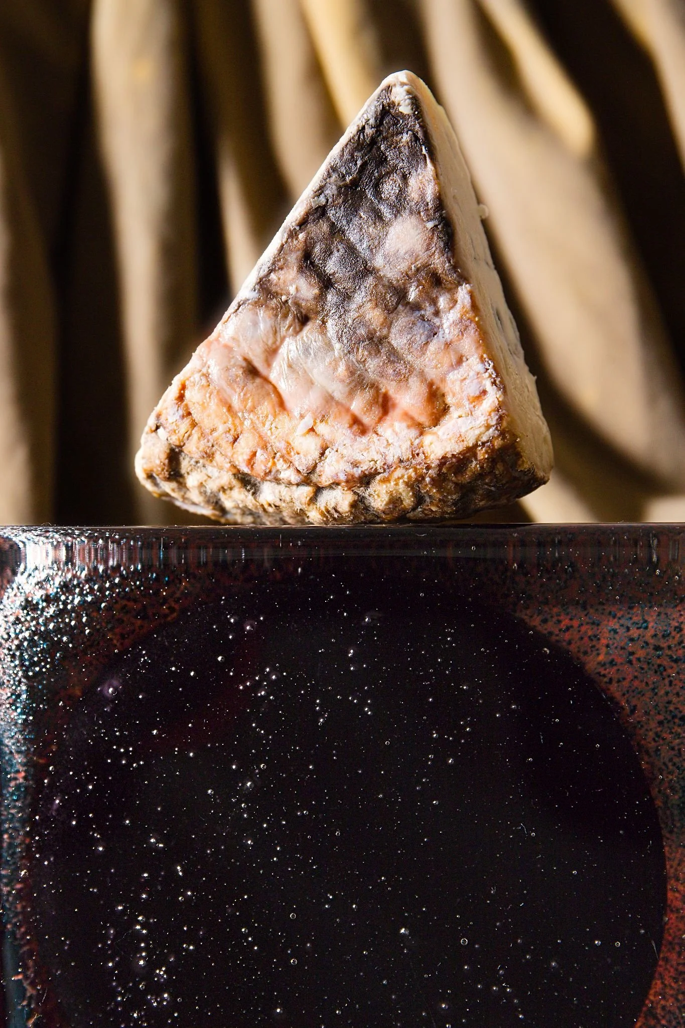 A triangle slice of textured brie cheese sitting on top of a glass brick with oxidised metals inside.