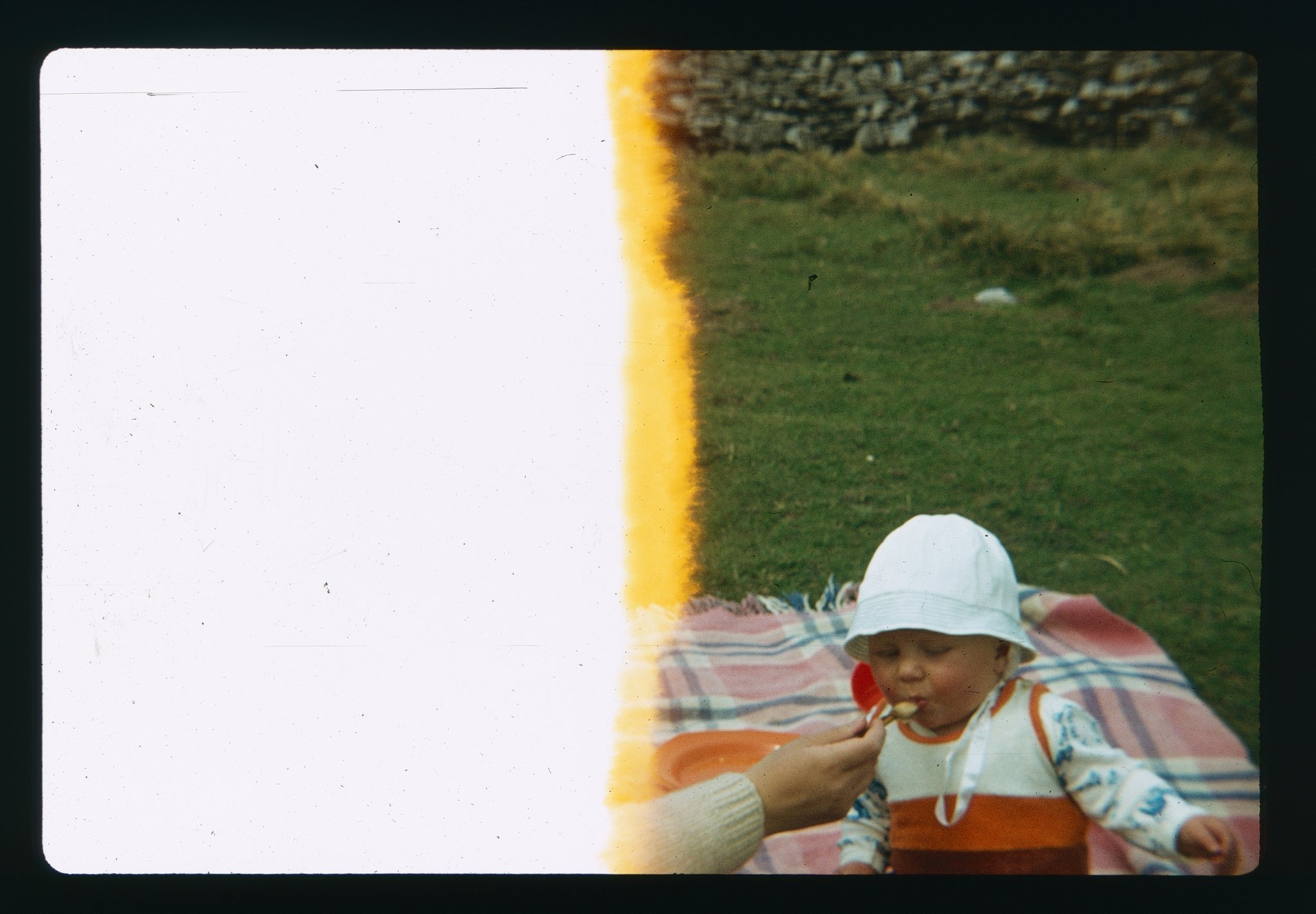 Half exposed photo of a baby on a picnic blanket being spoonfed.