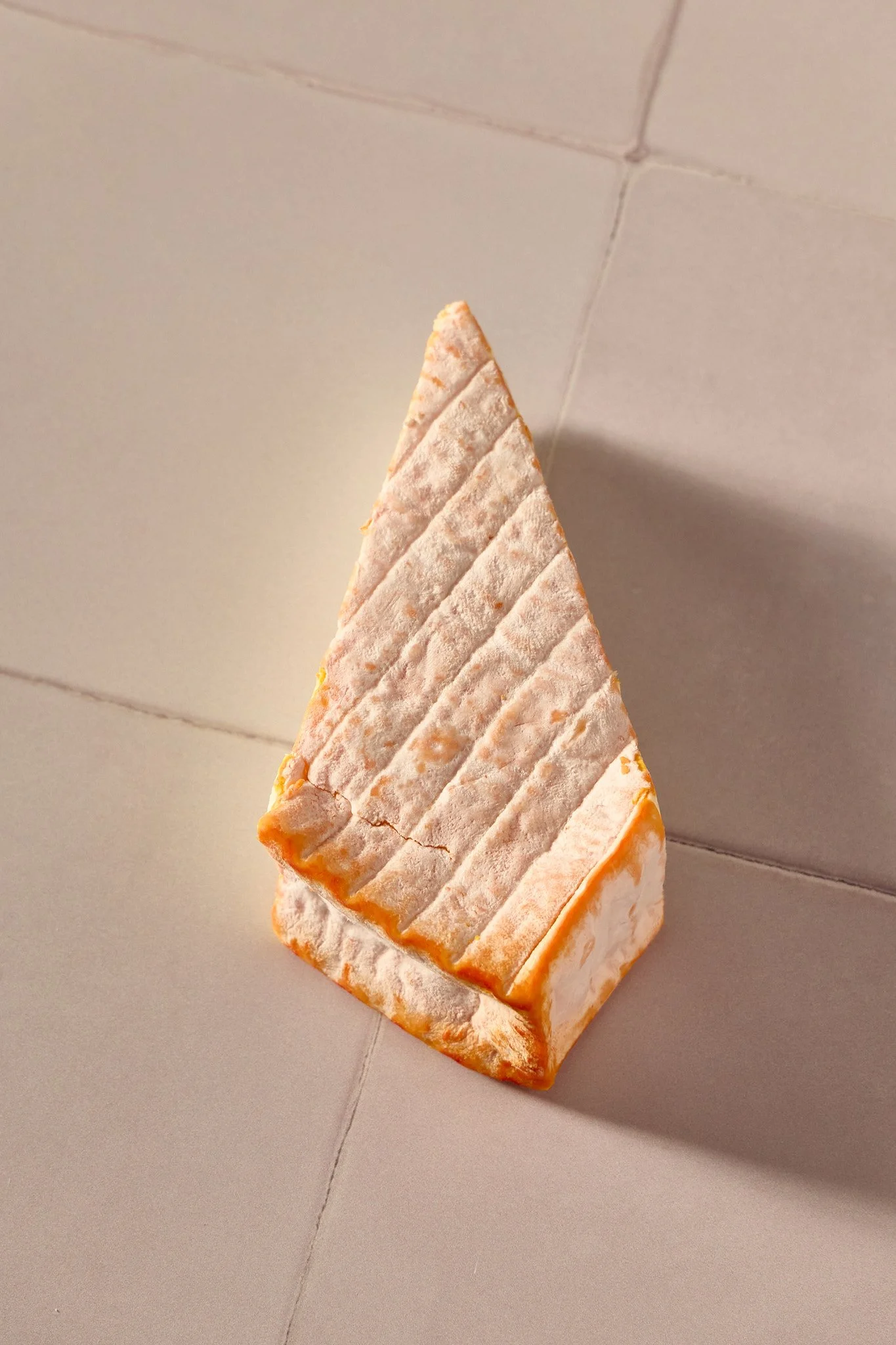 Soft white cheese with orange mould edging sitting on a white tiled background.