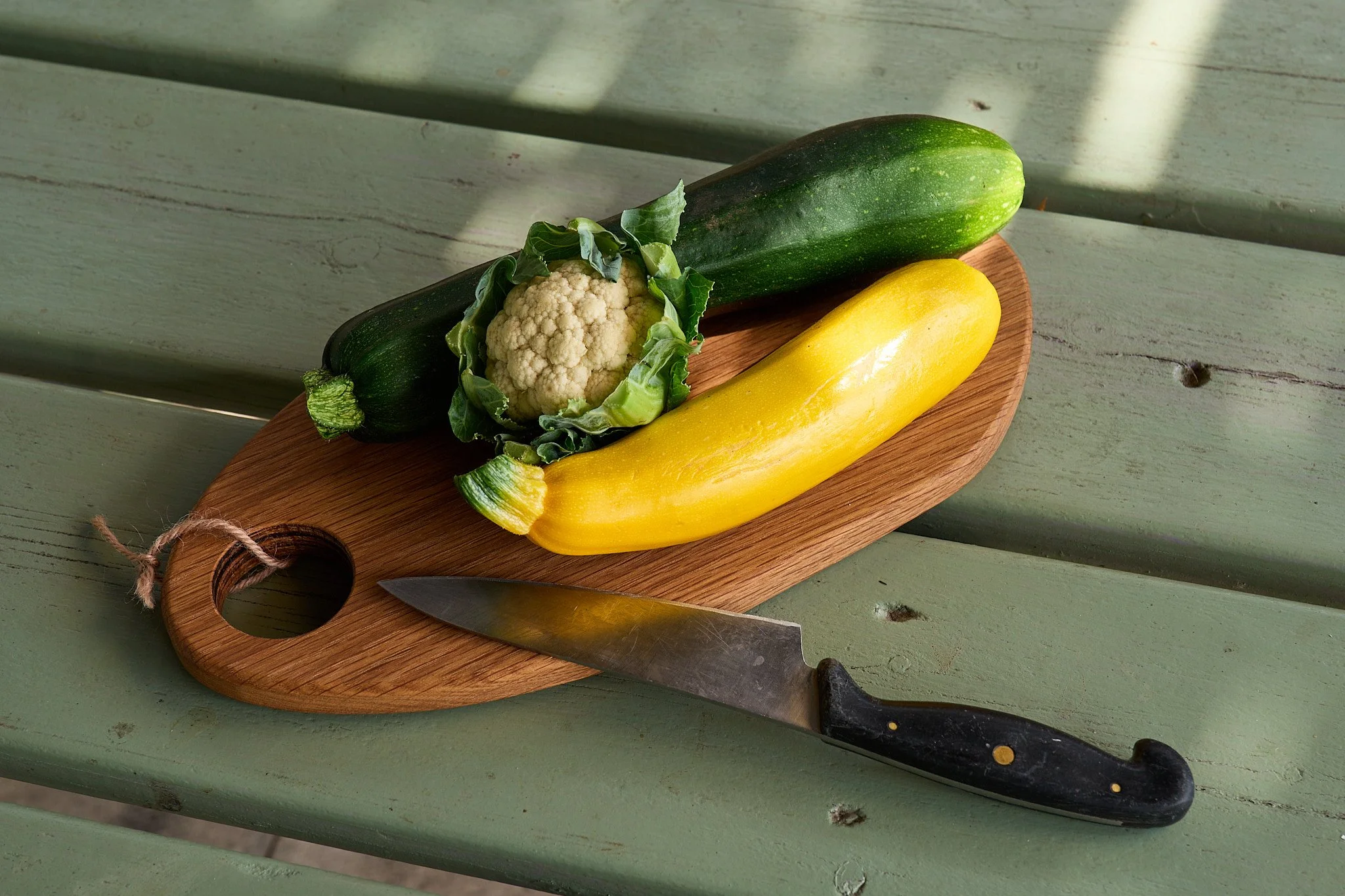 Chopping board with green and yellow courgettes and a tiny cauliflower.