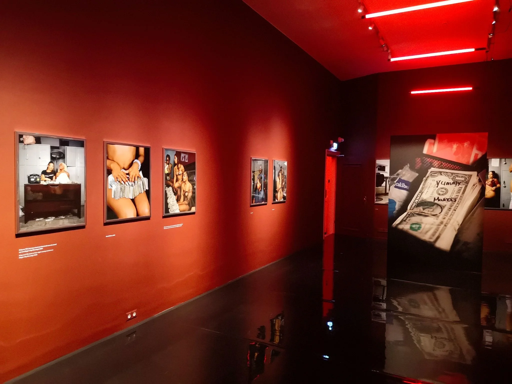 A dark red room with a polished featuring a photo exhibition by Hajar Benjida at Foam Amsterdam. The photos are a mixture of semi naked women and piles of money.