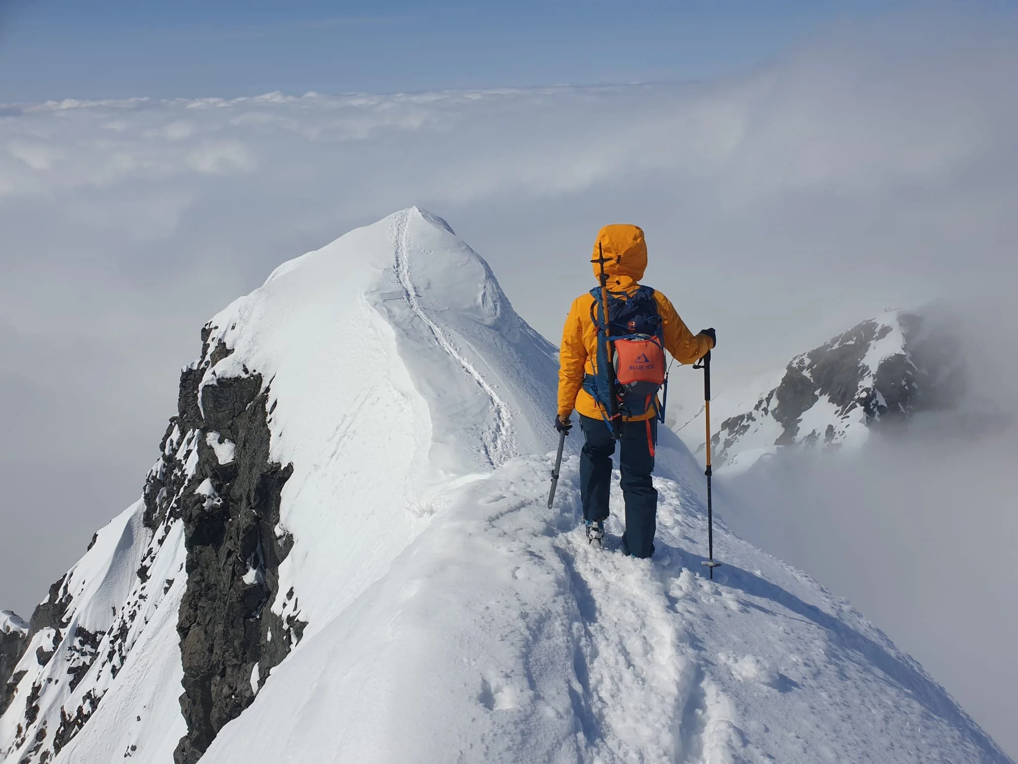 To fjellklatrere på snødekt fjelltopp med utsikt over snødekte fjell og skyer.