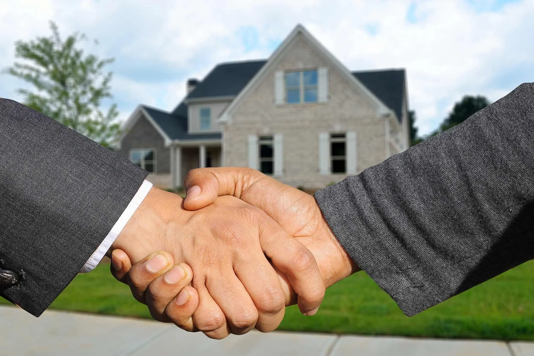 Two people shaking hands in front of a house to finalize a home sale.