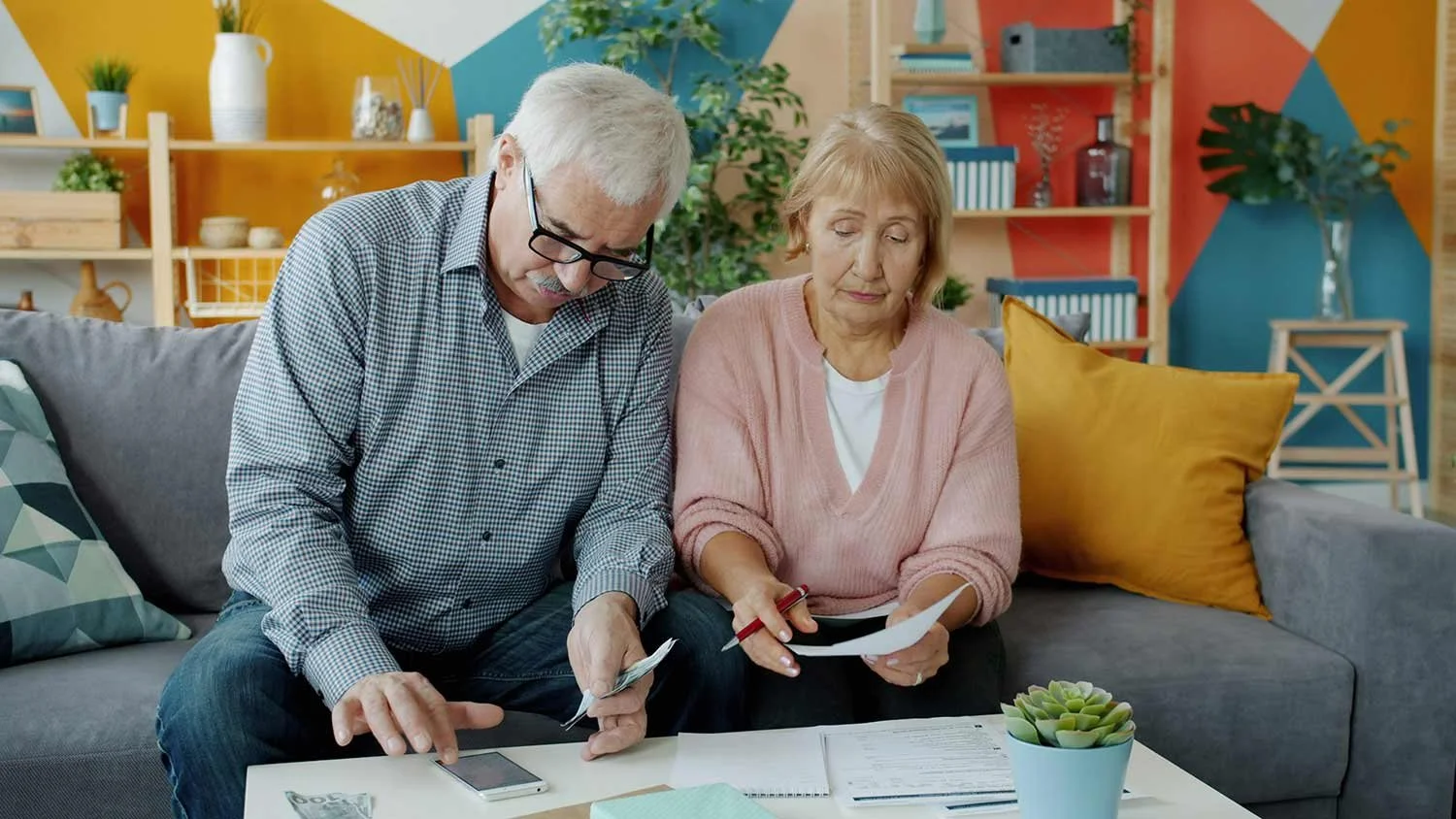 An older couple sitting on a couch reviewing paperwork and bills together.