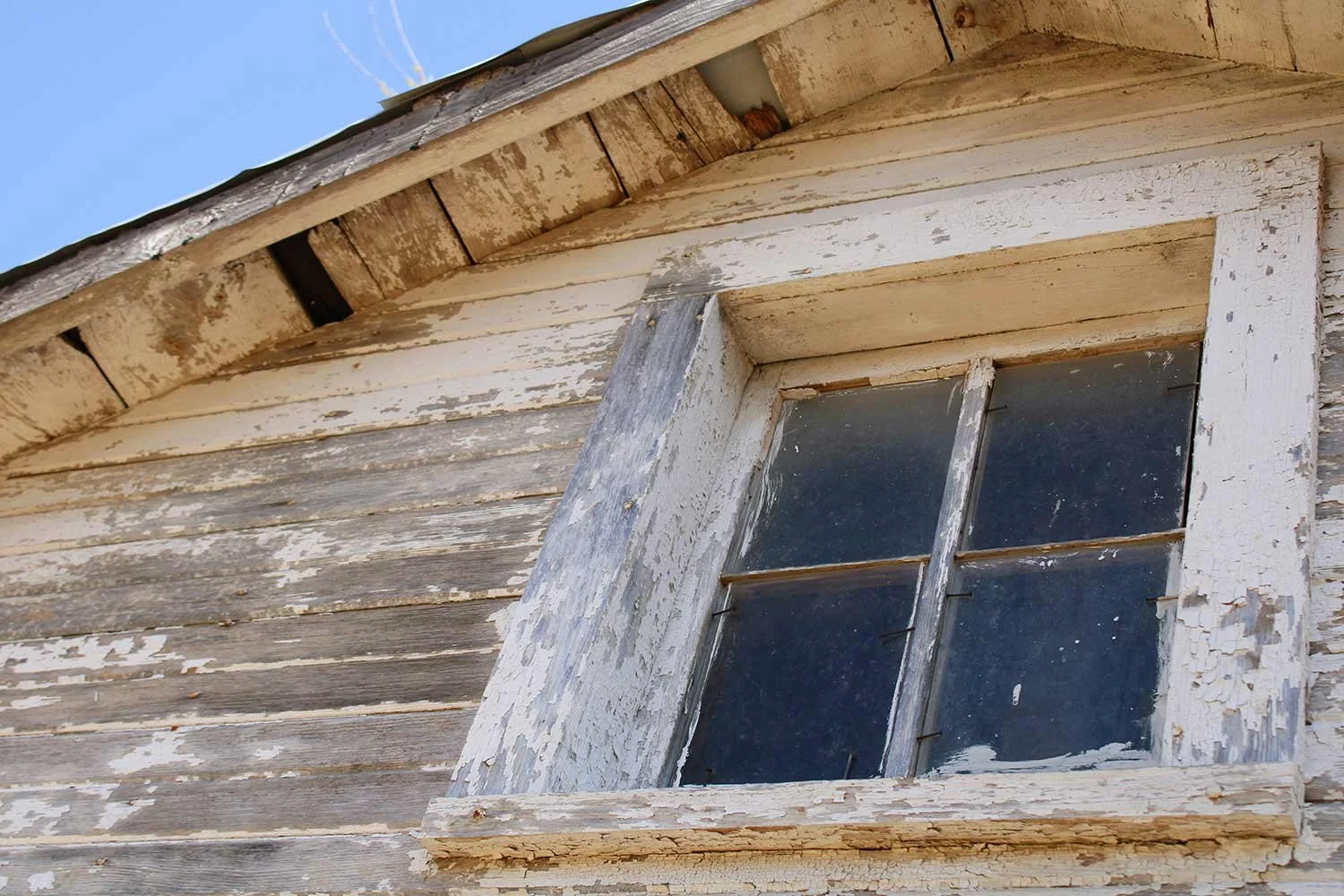 A close-up of a weathered window with peeling paint on an older home.