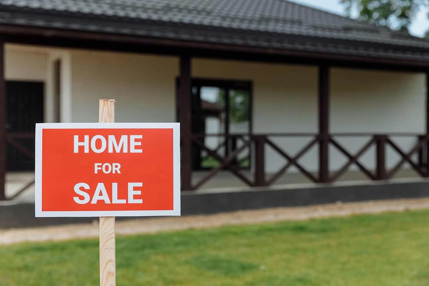 A home for sale sign posted in the front yard of a house.
