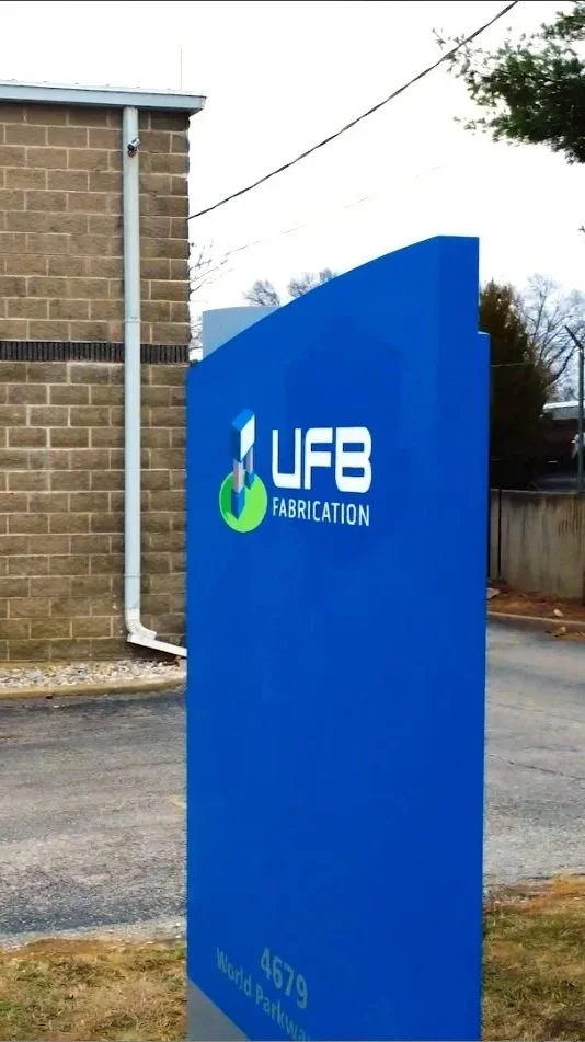 Blue sign with UFB Fabrication logo and the address 4679 World Parkway Drive.