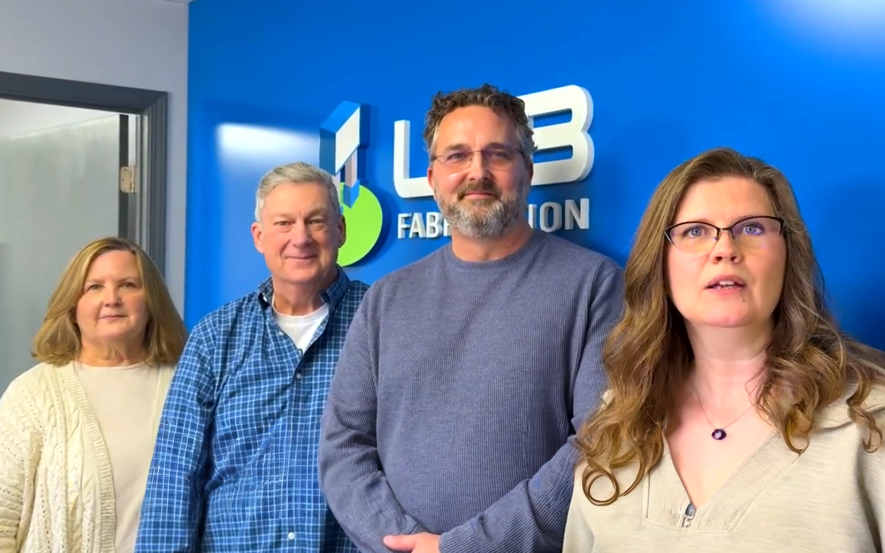 Four people standing in front of a blue wall with a logo and the words "L3 Fabrication."
