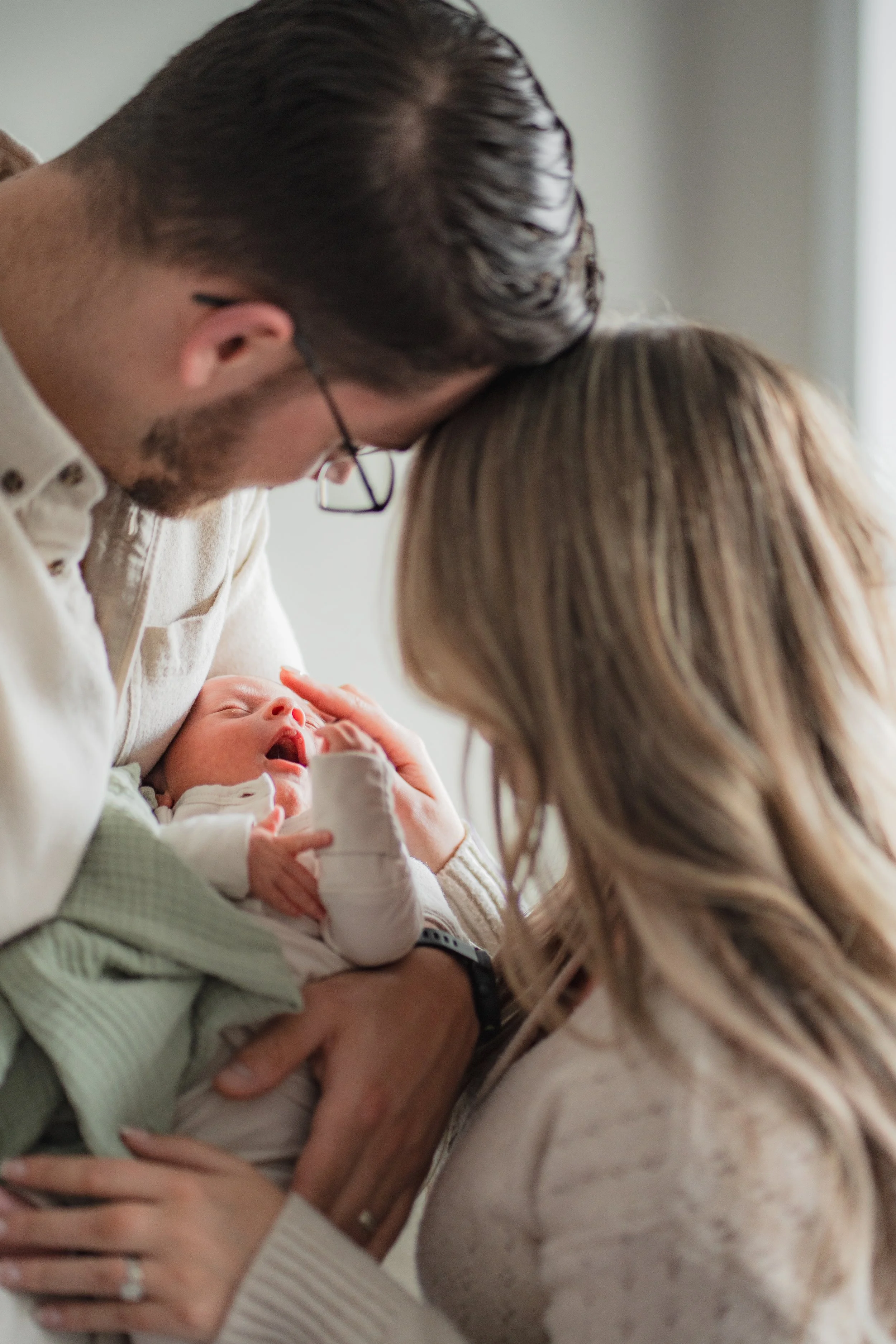 A family with a newborn baby, the father and mother gently touching the baby's face, creating a tender moment.