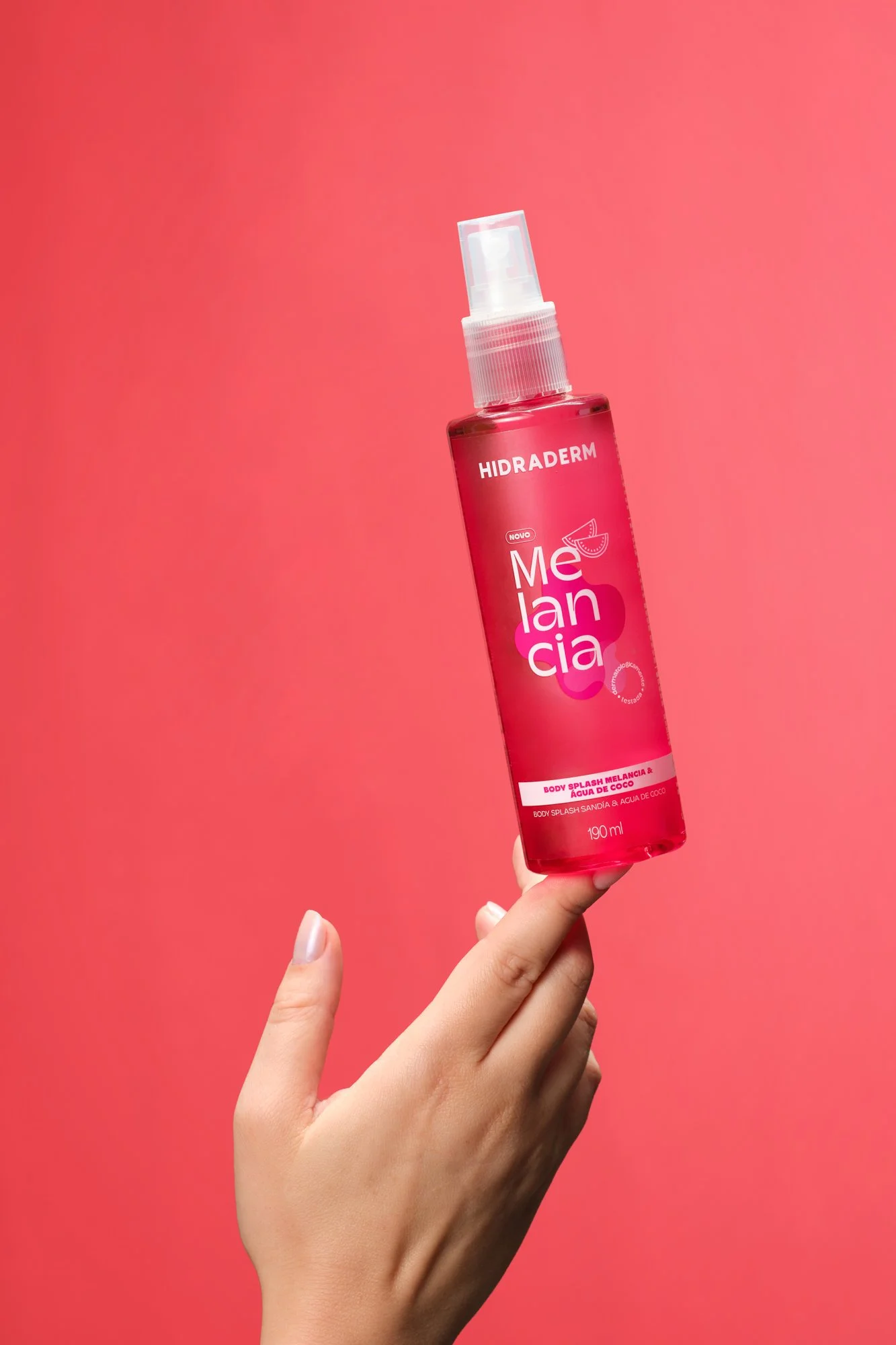 Pulso segurando uma garrafa de hidratante corporal com fundo rosa.