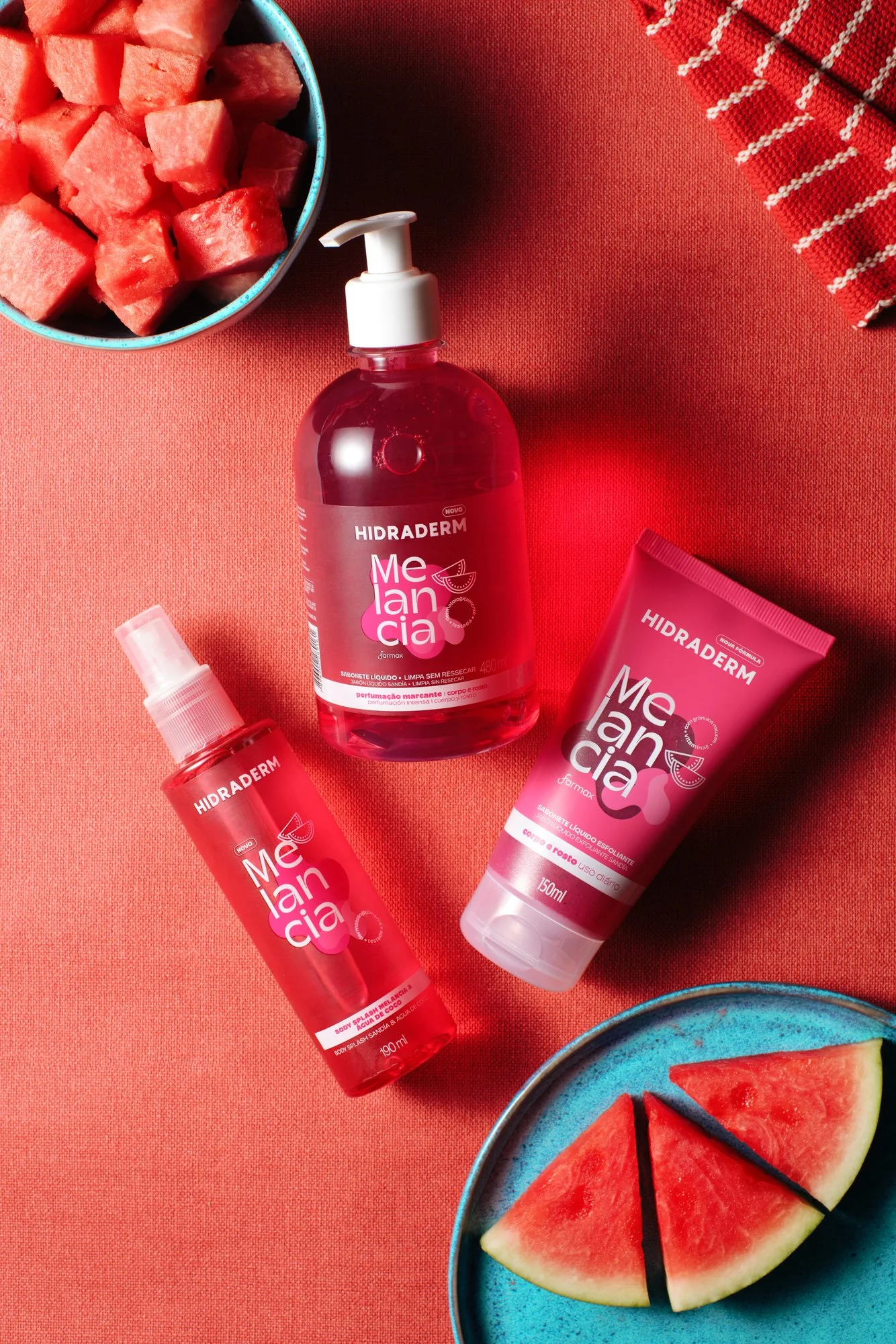 Produtos de cuidado com a pele hidratante Melancia, incluindo sabonete líquido, spray corporal e creme, ao lado de fatias de melancia em pratos azuis.