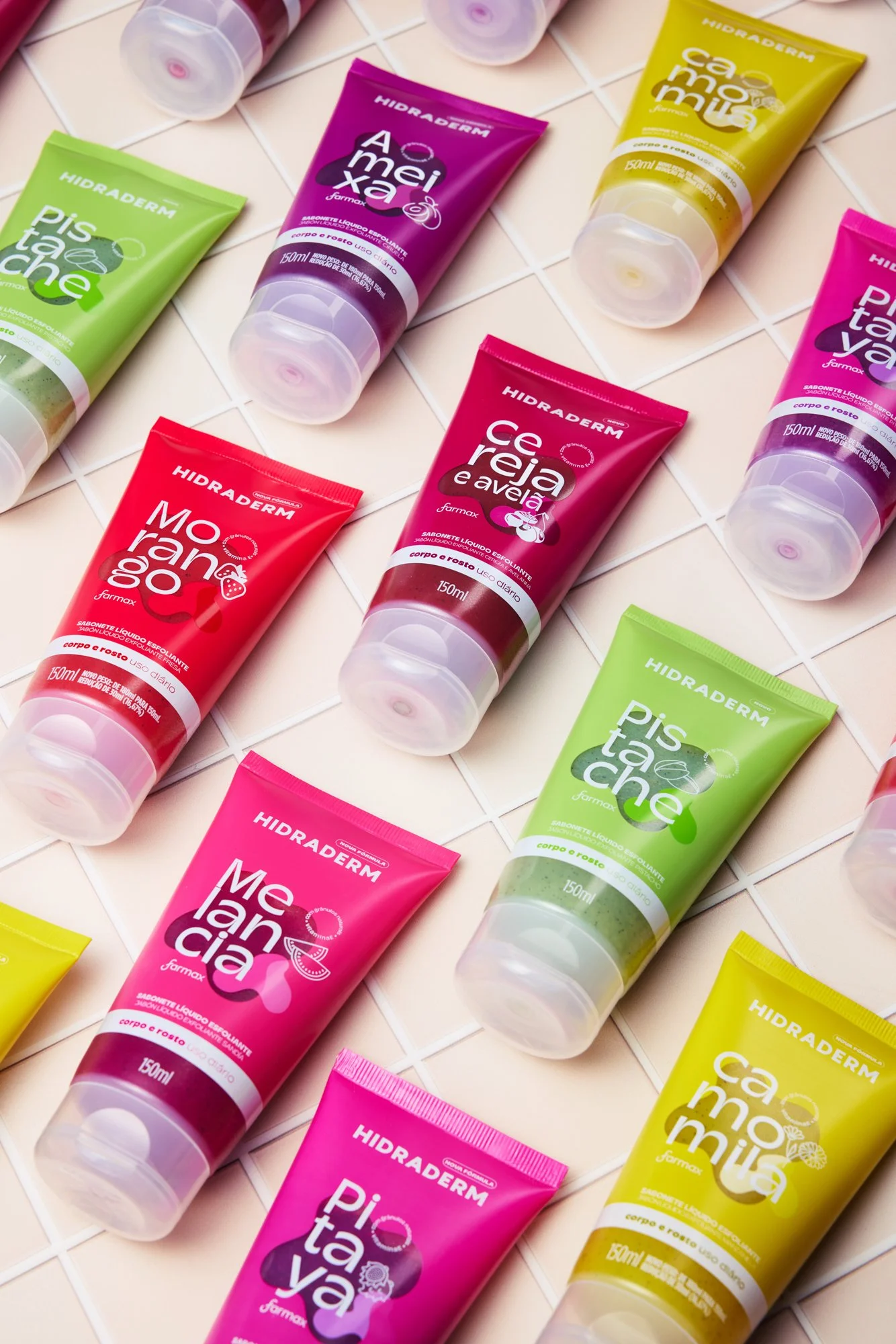DIVERSOS SABONETES LÍQUIDOS HIDRADERM EM EMBALAGENS COLORIDAS, DISPONÍVEIS EM FLORES, FRAMBOESA, PITAIA, LIMÃO, E MANGA, SOBRE Azulejos BRANCOS.