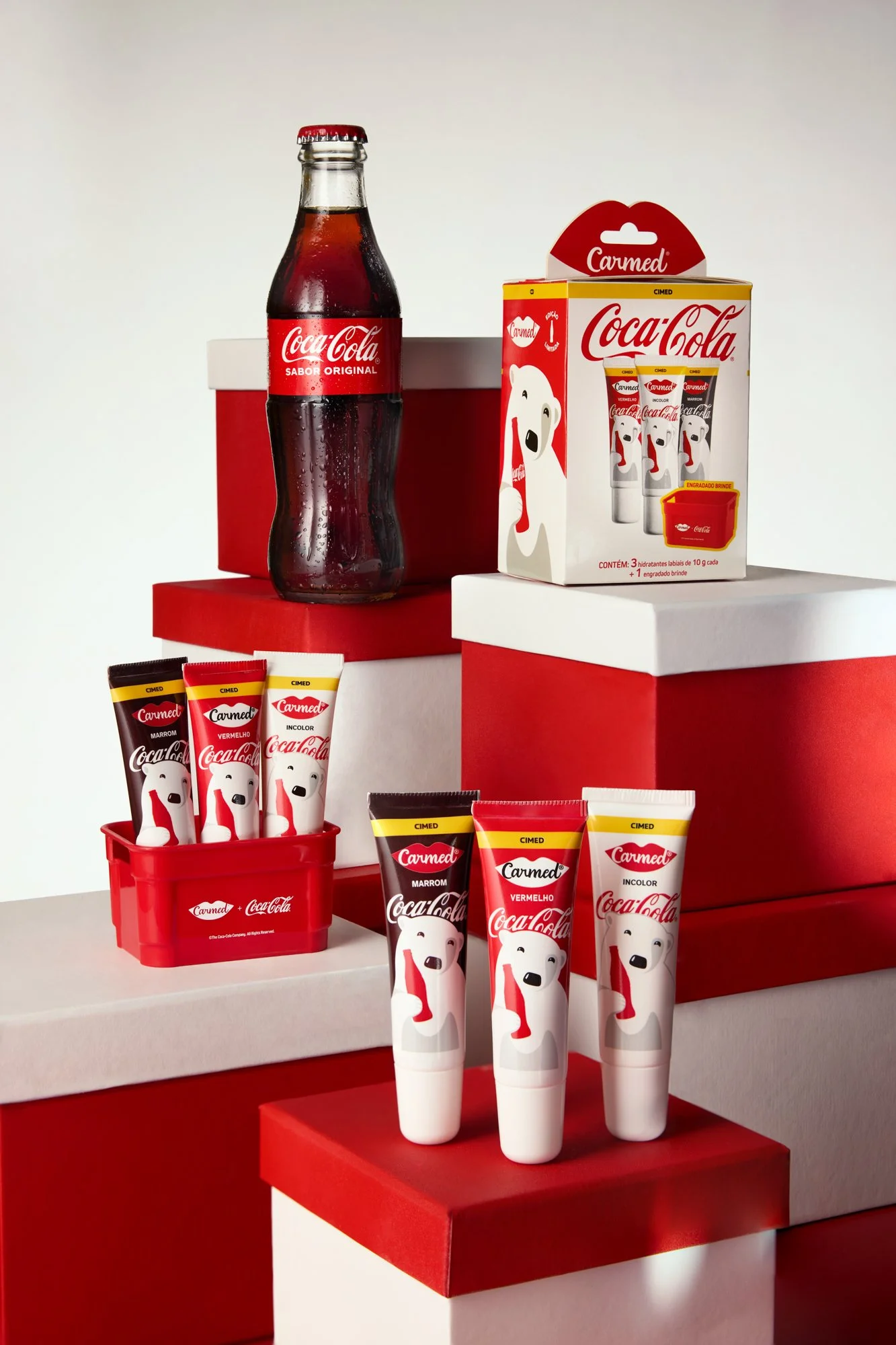 Produtos de Coca-Cola incluindo uma garrafa de refrigerante, caixas de cremes dentais com tema de urso polar, e um pacote de embalagem com três cremes dentais de sabores diferentes, decorados em caixas vermelhas e brancas com tema polar.