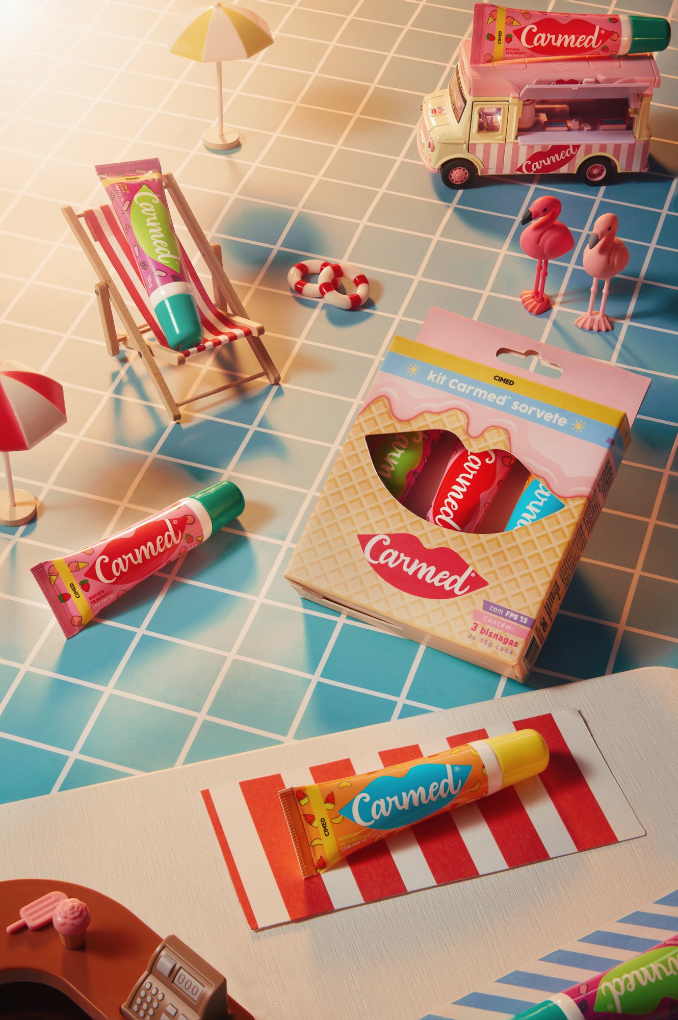 Brinquedos de plástico e papel decorativos de verão, como sorvetes, flamingos, guarda-sol, cadeira de praia e caminhão de sorvete em um cenário simulado de praia com mesa de guarda-sol.