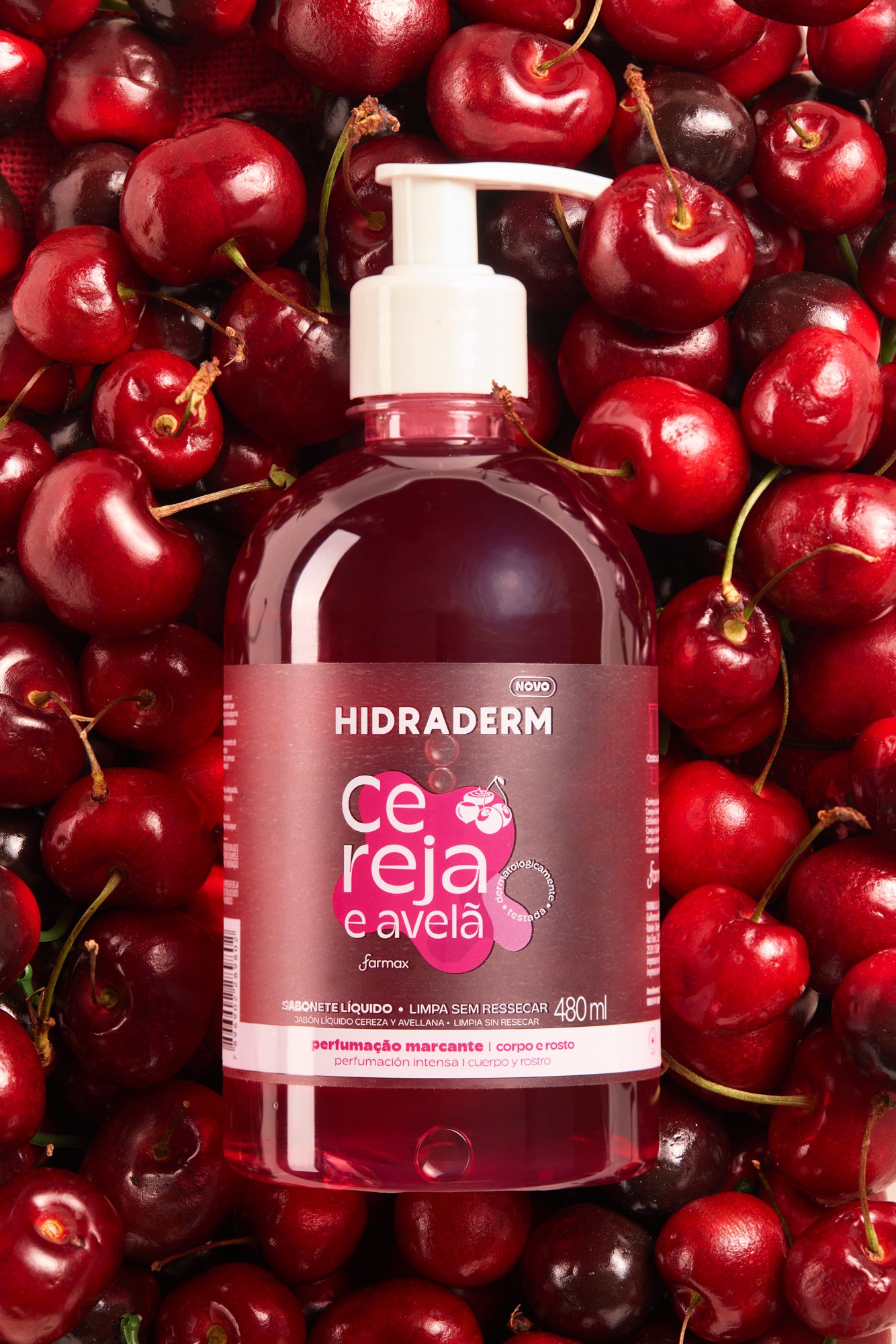 Frasco de sabonete líquido com rótulo rosa e branco, rodeado de cerejas e amoras vermelhas.