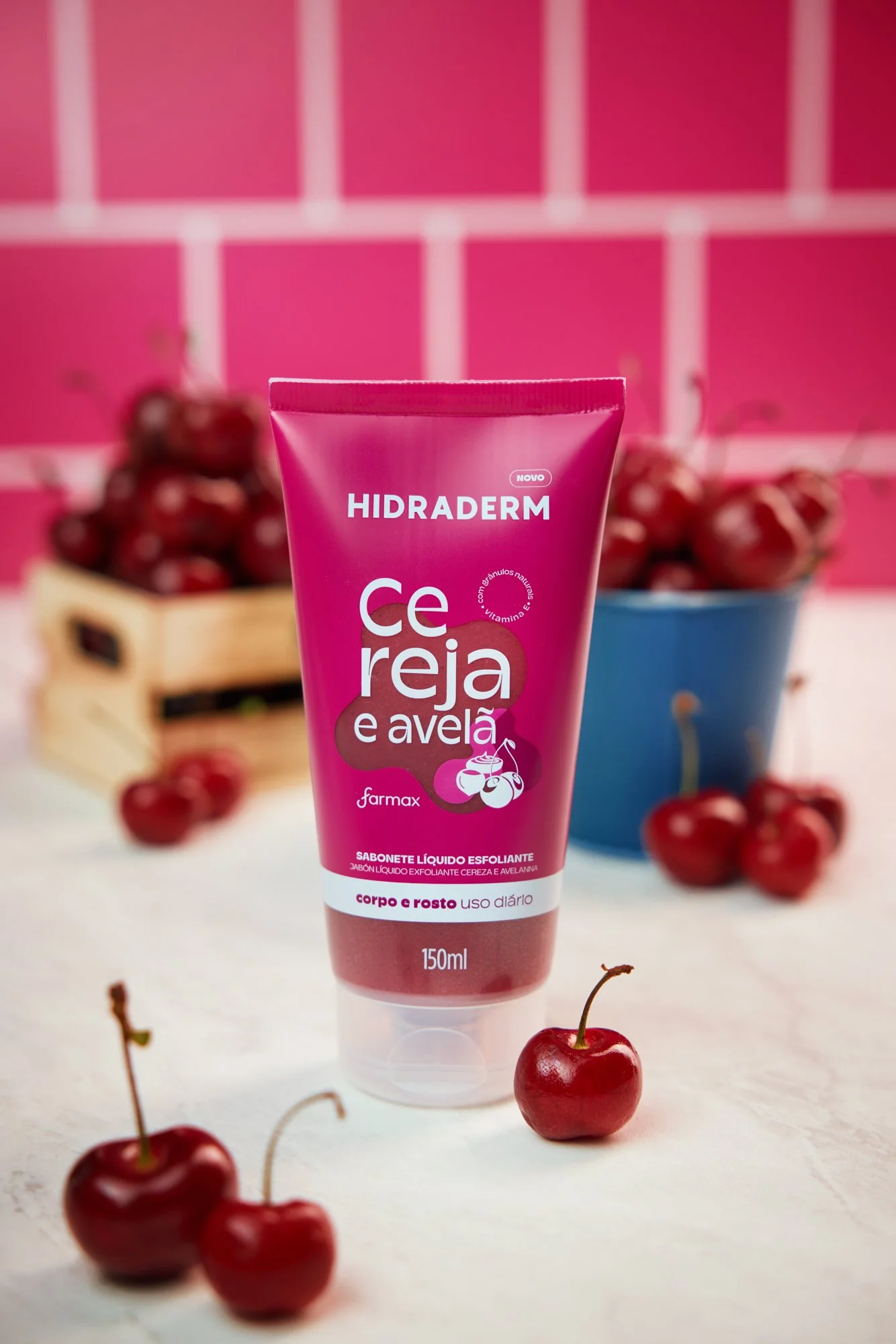 Um frasco de sabonete líquido esfoliante com sabor de cereja e amora, da marca Farmax, em destaque na frente da imagem, com cerejas ao redor da embalagem e uma tigela cheia de cerejas ao fundo, tudo sobre uma superfície clara com uma parede de azulej