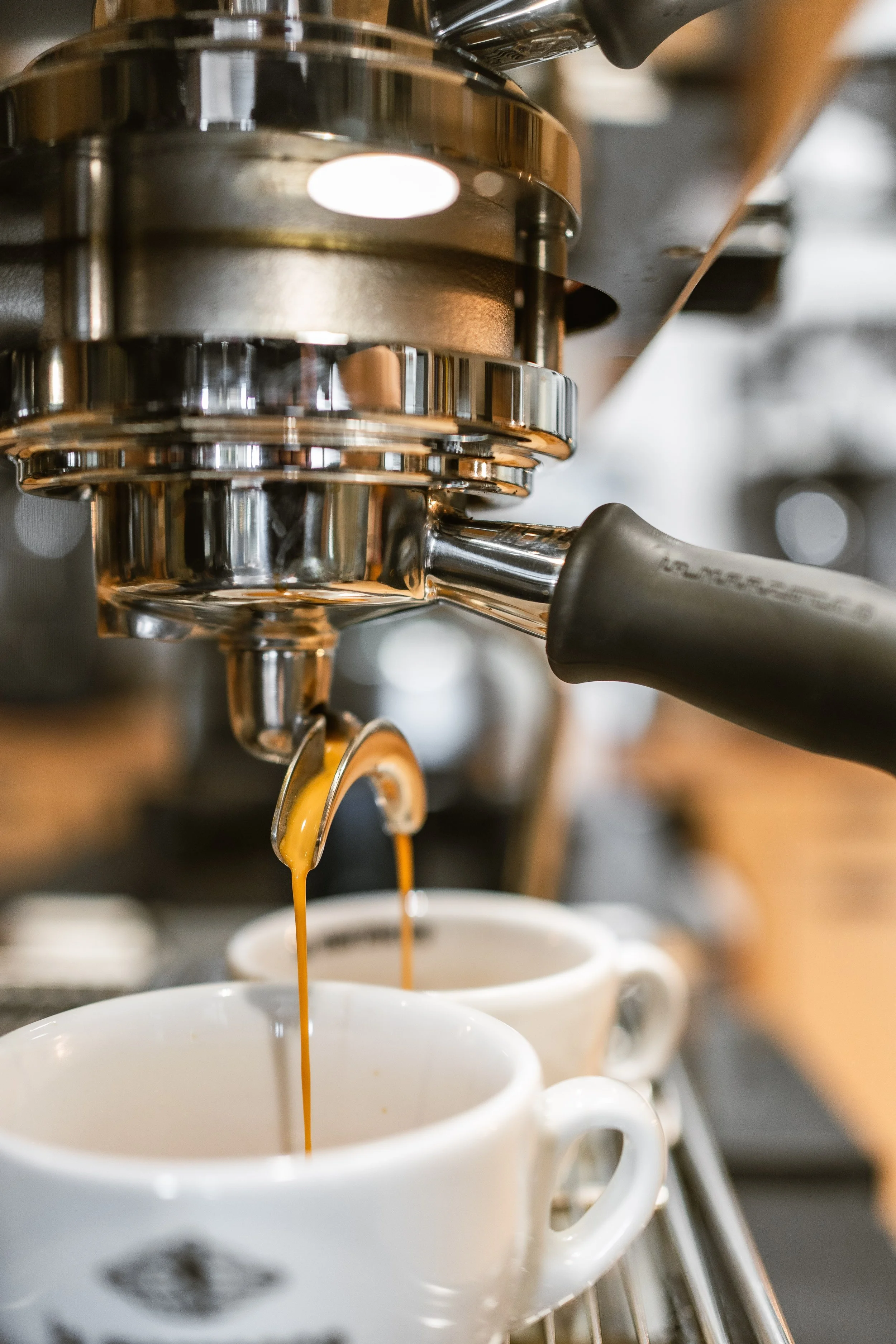 Zwei Espressi werden mit einer Espressomaschine in weiße Tassen extrahiert, sichtbare Details der Maschine und fallender Kaffee.