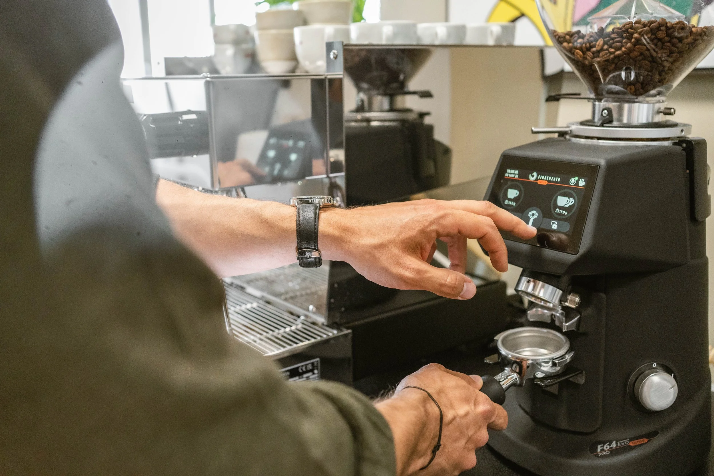 Hand touching Bedienfeld einer Kaffeemühle mit Kaffeebohnen im Behälter daneben.
