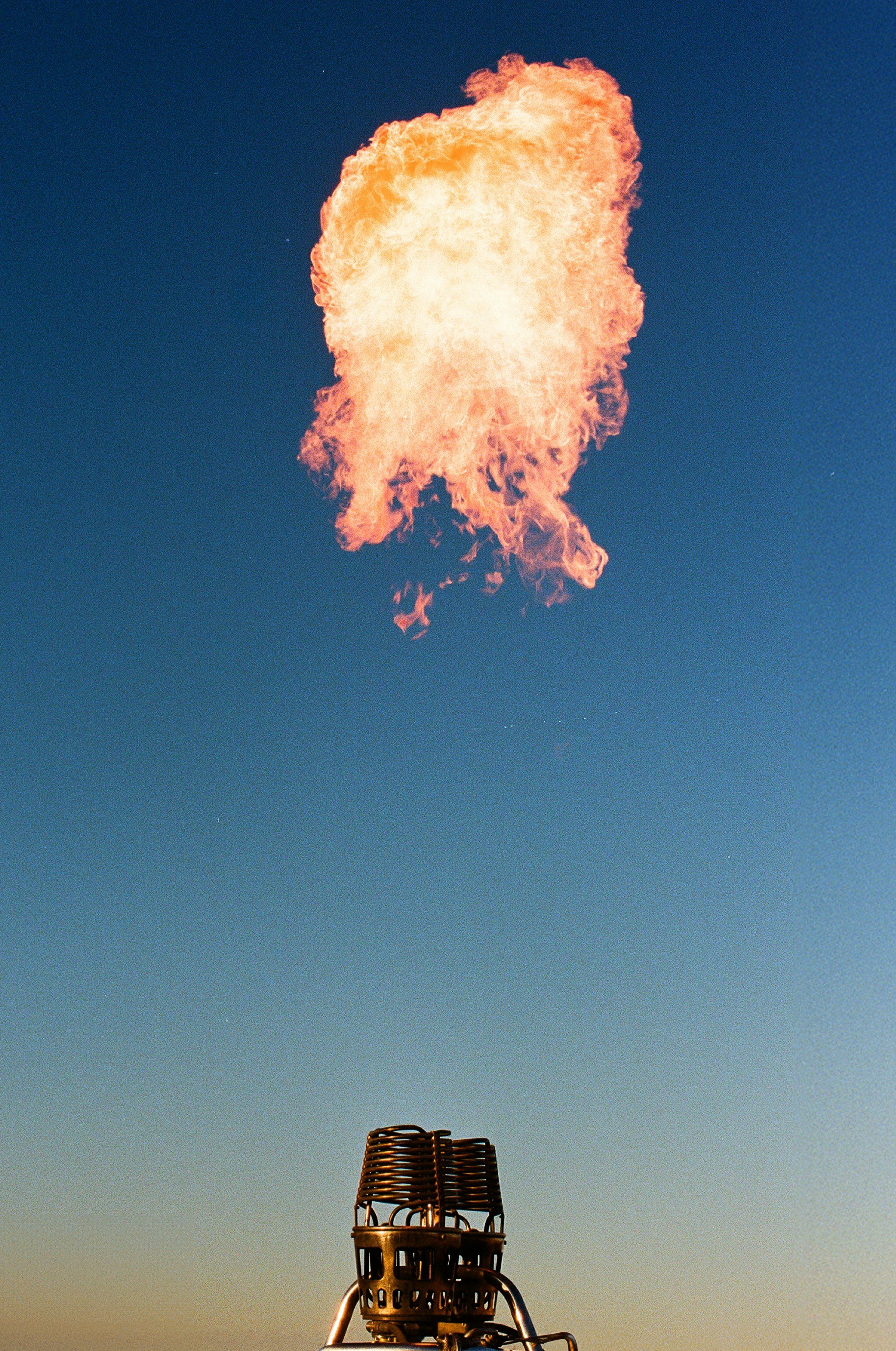 An outdoor scene with a hot air balloon basket at the bottom and a large explosion or fireball in the sky above, against a clear blue sky.