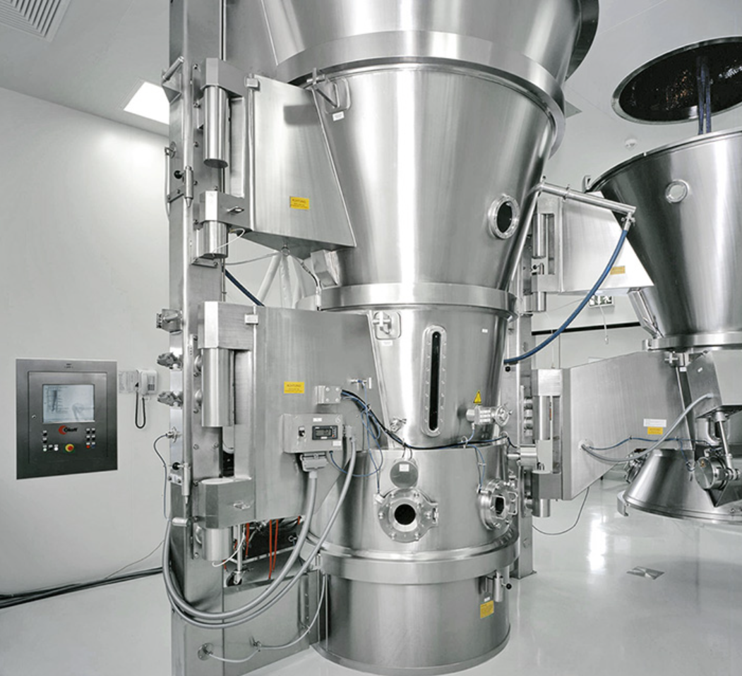 Large metallic industrial machine with pipes and controls in a clean, modern facility.