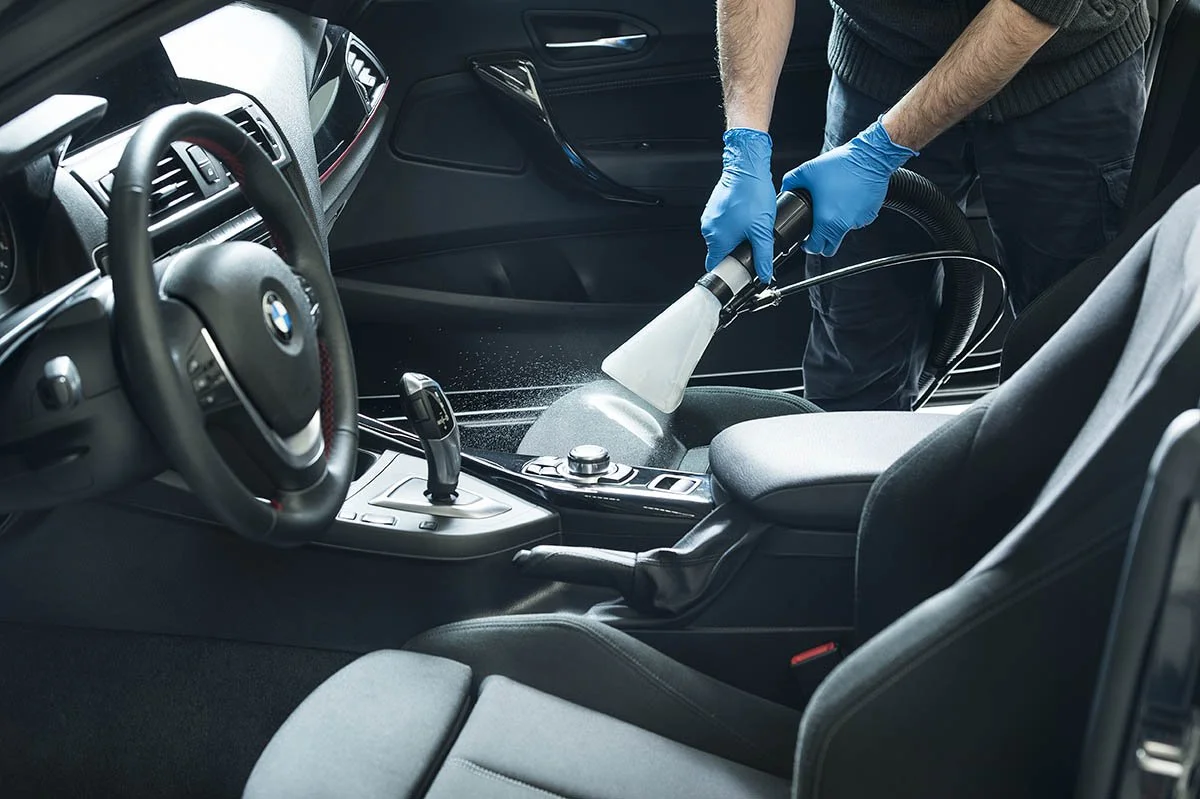 Nettoyage intérieur d'une voiture avec un appareil à vapeur, personne portant des gants bleus.