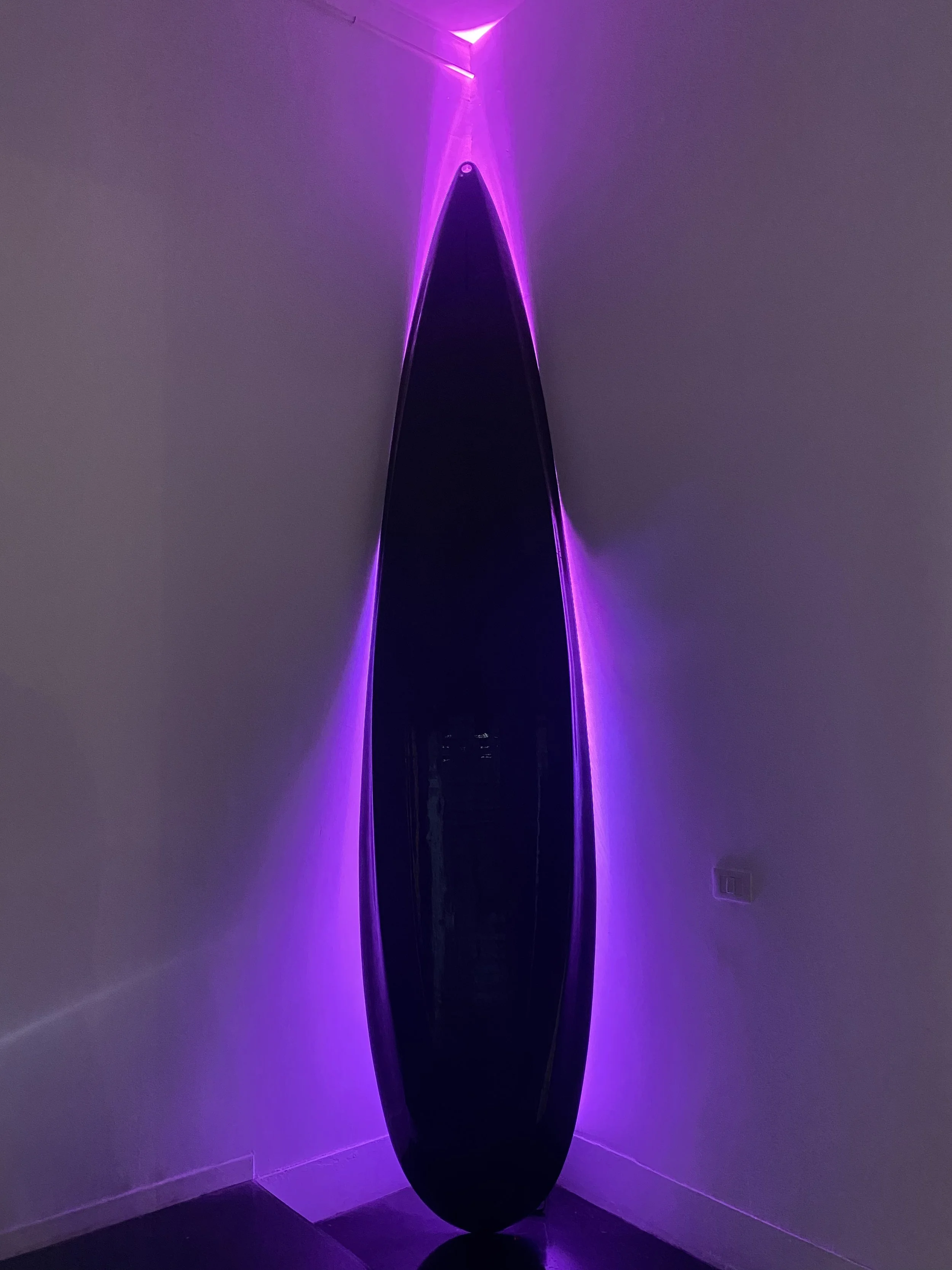 Black surfboard with purple LED lights on a wall in a dimly lit room.