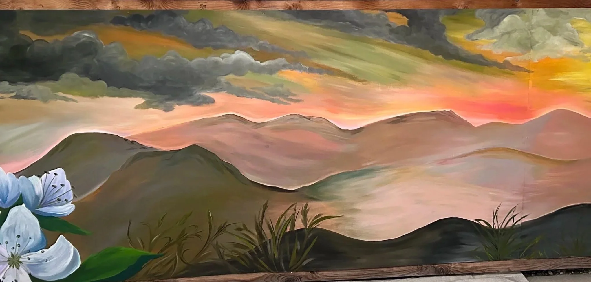 A colorful landscape painting of mountains during sunset with dark clouds and a hint of sunlight on the horizon, and white syringa flowers with green leaves in the foreground.