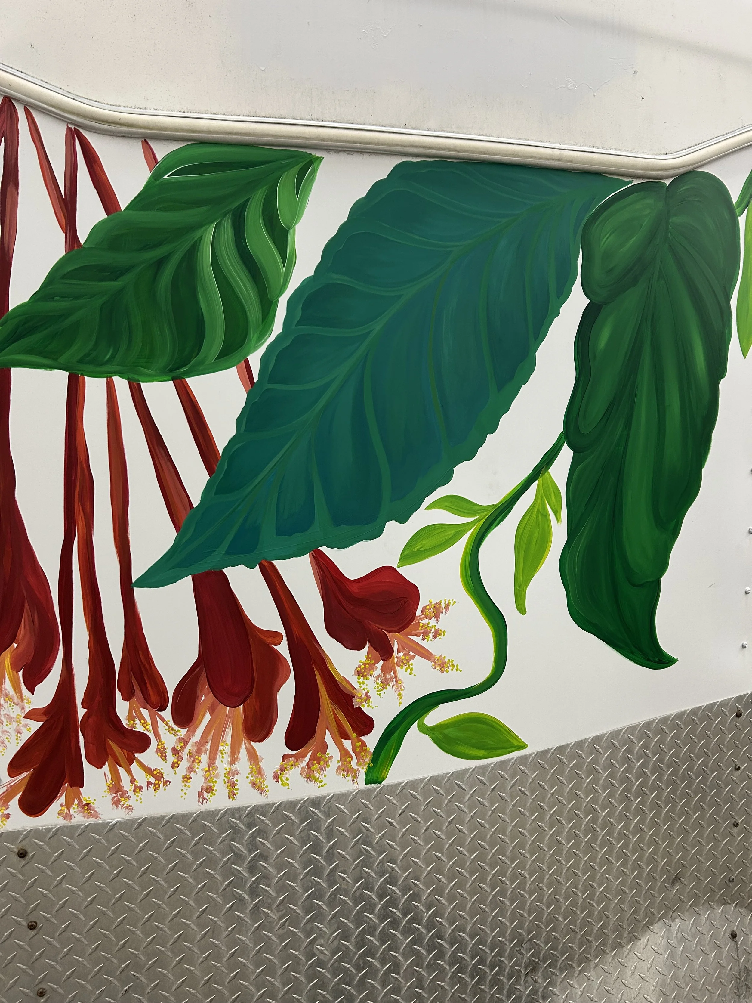 Colorful mural of large green leaves with red and yellow flowers and stems on a white wall.
