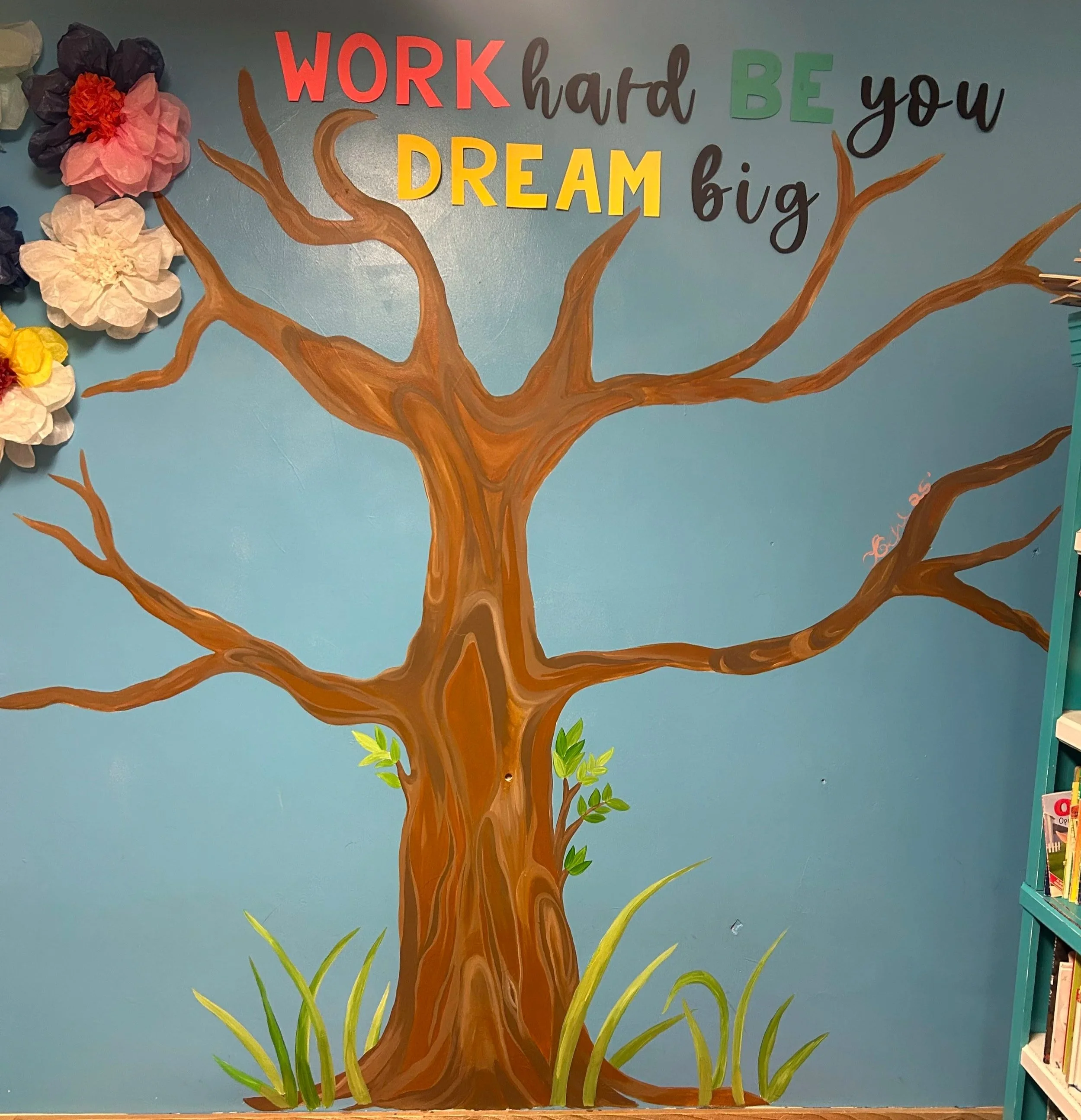 Decorative wall with painted tree and motivational words, including 'WORK hard BE you DREAm big' and colorful paper flowers on the left