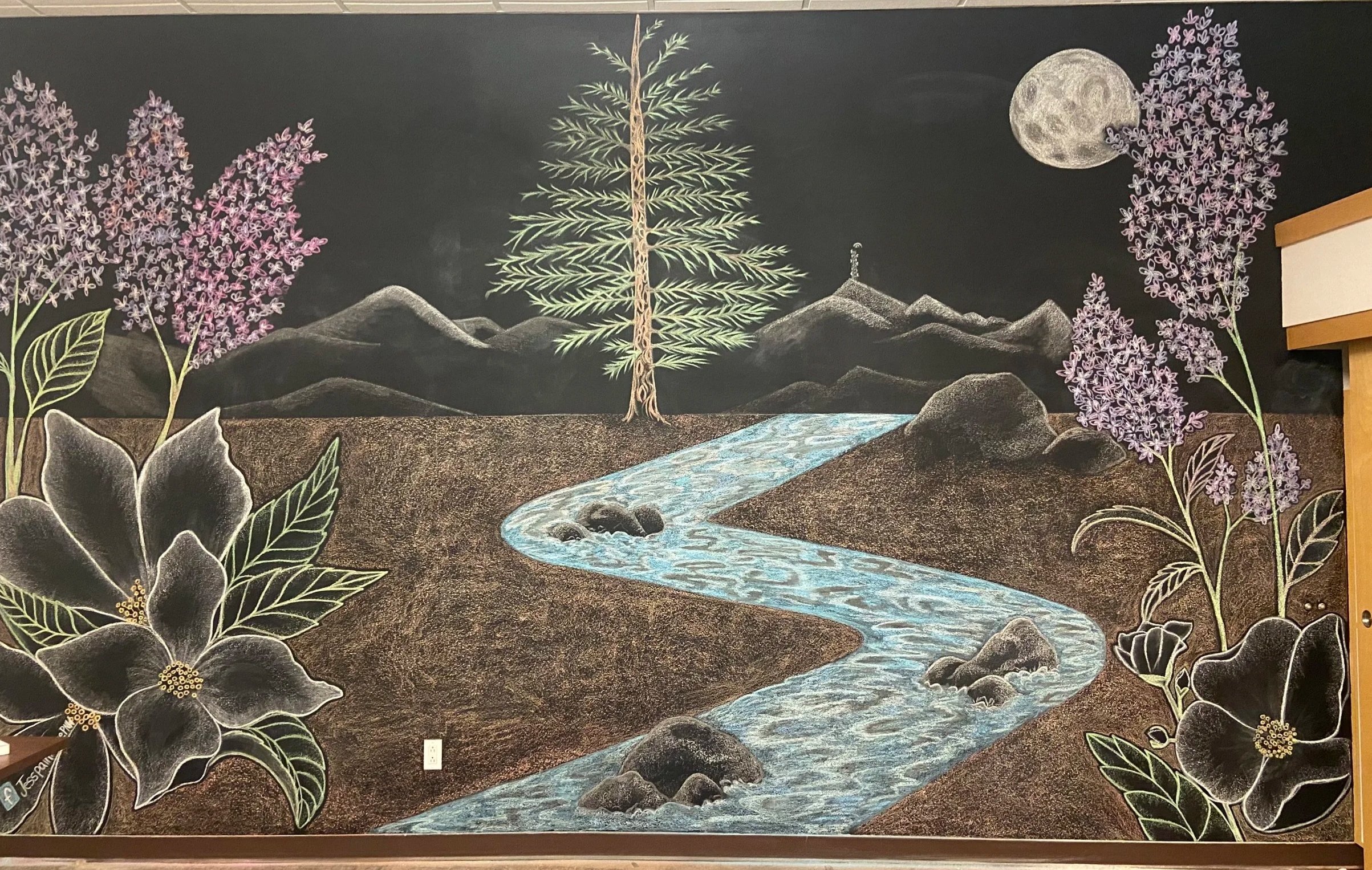 Chalkboard mural of a natural landscape featuring a stream, mountain peaks, a large moon in the sky, a central pine tree, and purple flowering plants in the foreground.